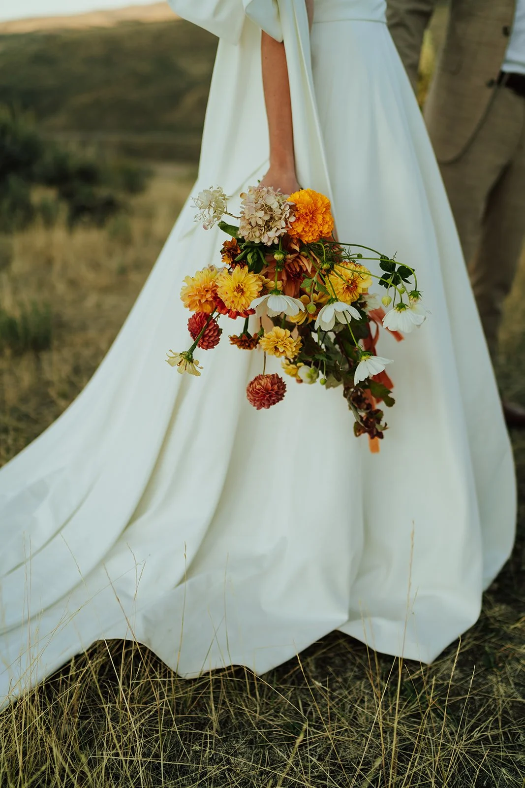 a bride holds her bouquet of white, yellow, and orange blooms next to the train of her wedding dress - photography by  Poise and Ivy Imagery