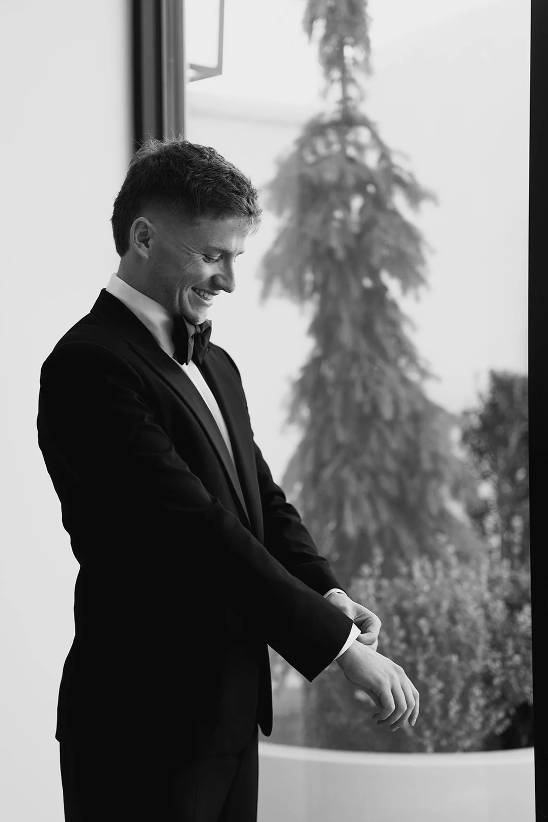 groom preparing for his wedding ceremony in front of a window viewing a green garden - photography by Poise and Ivy Imagery