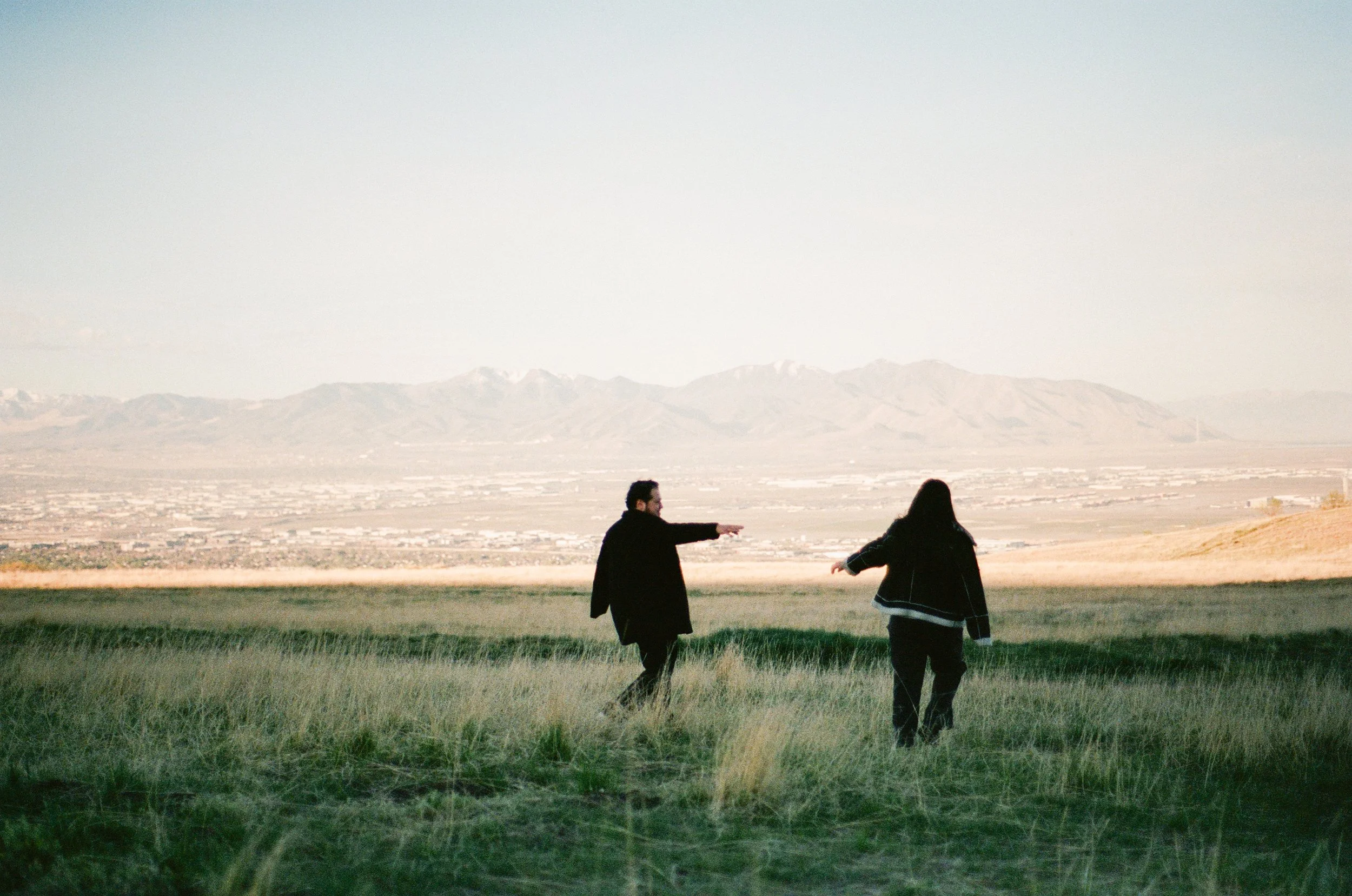 A couple stands together in a softly lit grassy field, photographed on color negative film by Poise and Ivy Imagery