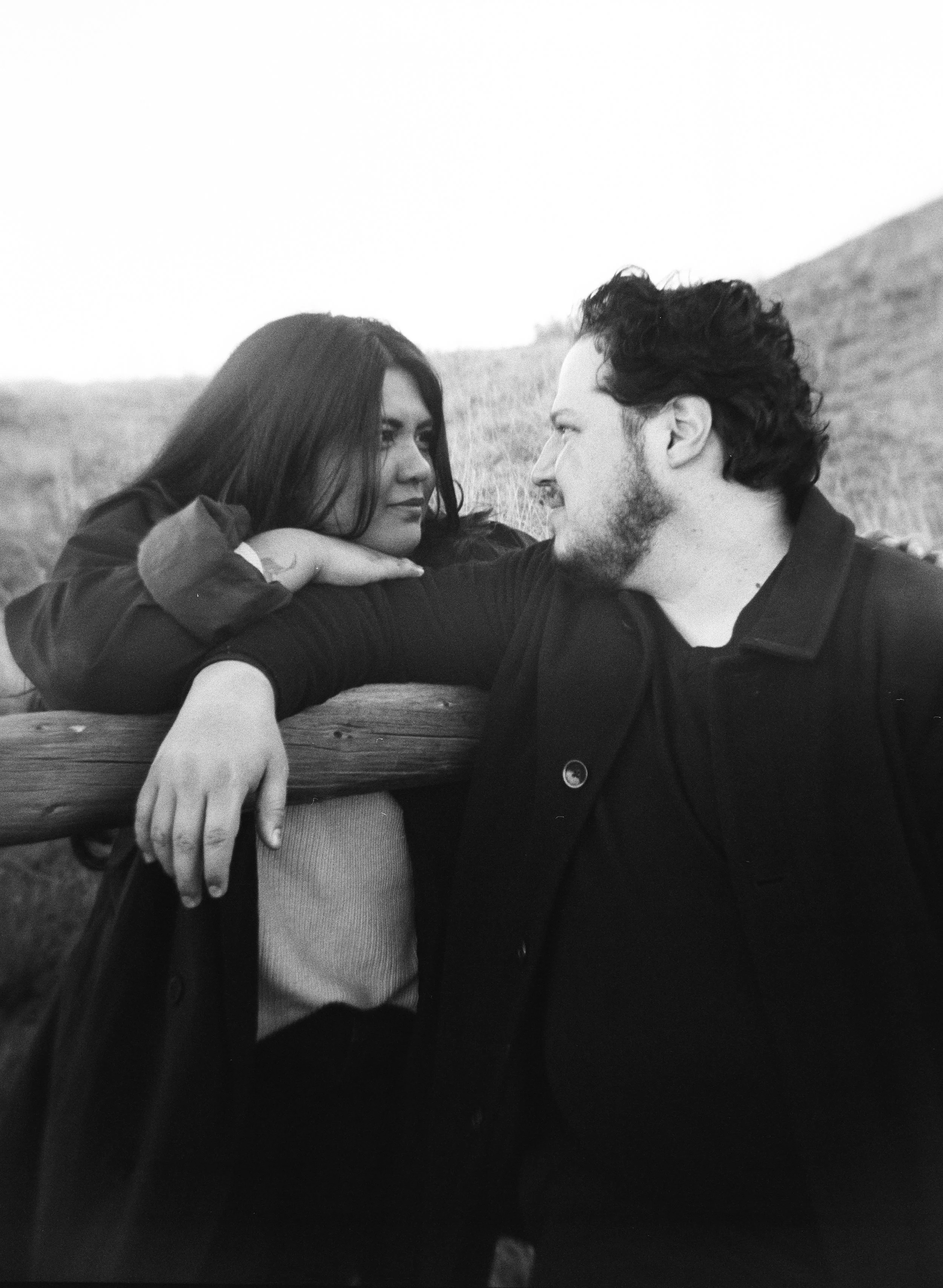 A couple stands together in a softly lit grassy field on black and white medium format film - photography by Poise and Ivy Imagery