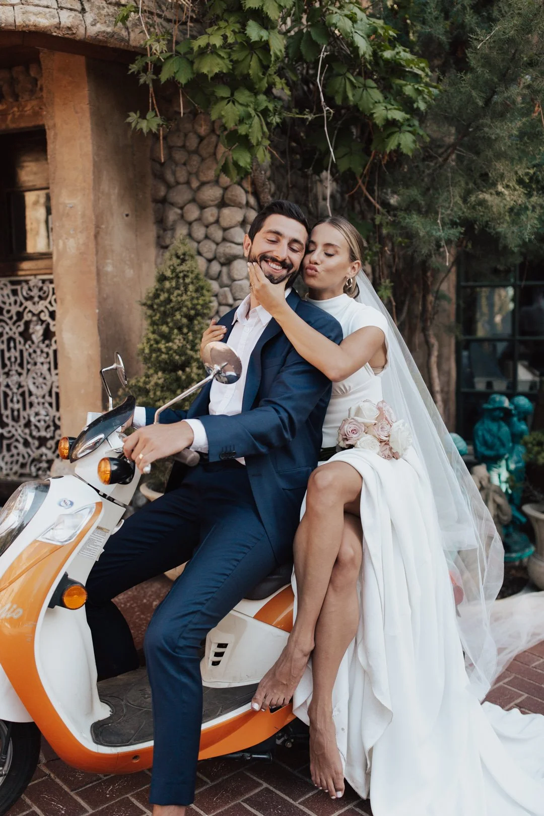 bride and groom in their wedding attire sit atop an orange vespa as they exit their wedding celebration at an Italian inspired villa - photography by poise and ivy imagery