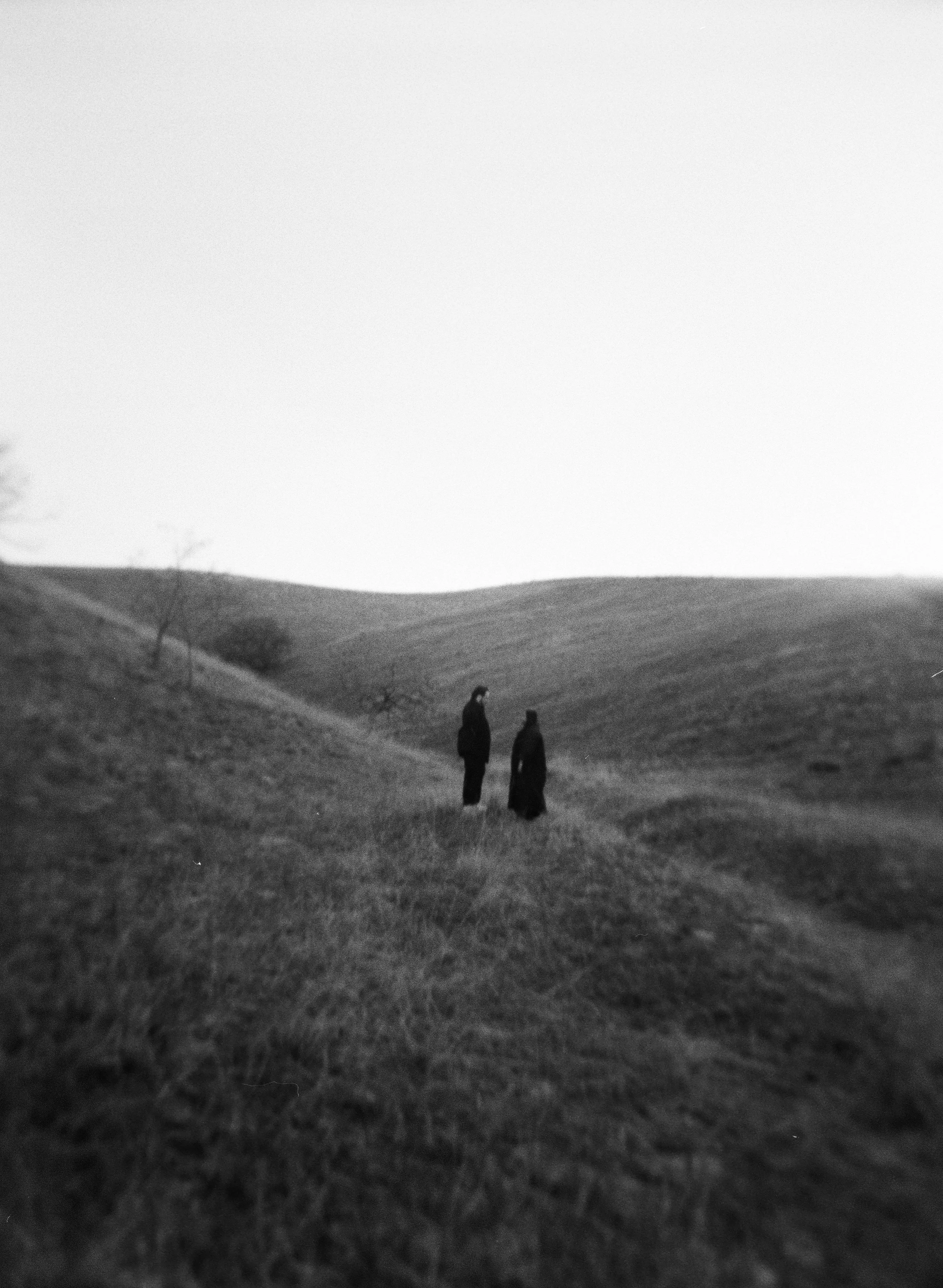 A couple stands together in a softly lit grassy field on black and white medium format film - photography by Poise and Ivy Imagery