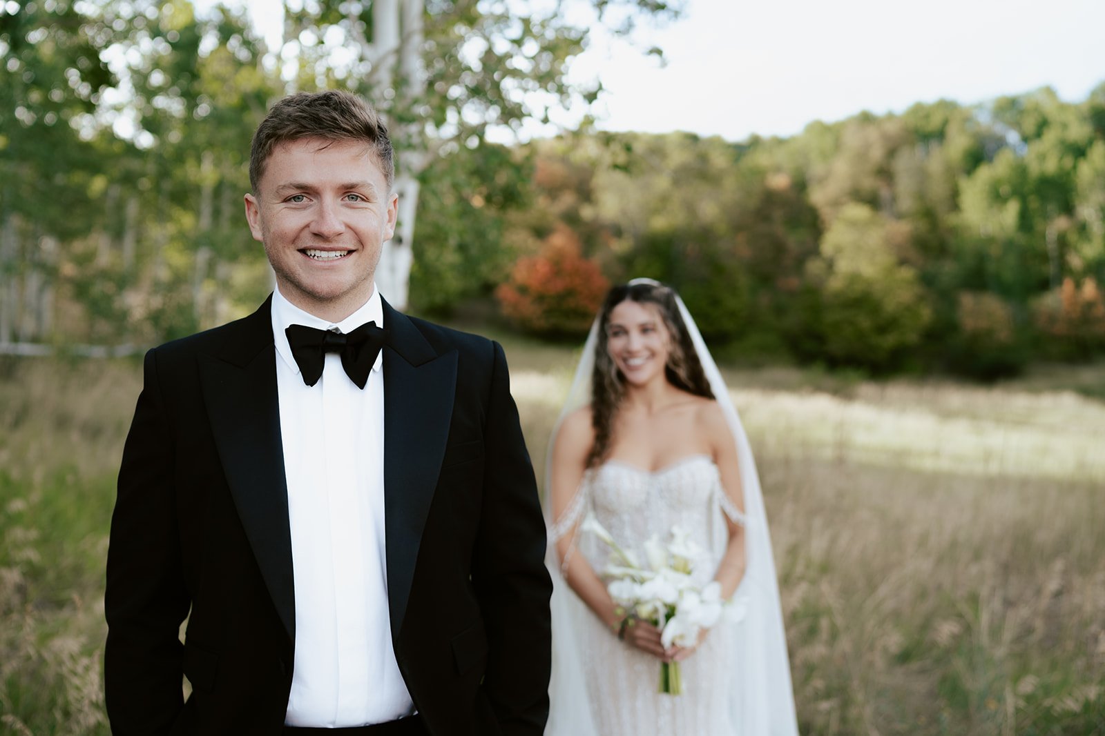 a bride and a groom stand together in a lush aspen grove. the bride wears a beaded wedding gown with a bridal veil and the groom wears a tuxedo. Photography by Poise and Ivy Imagery