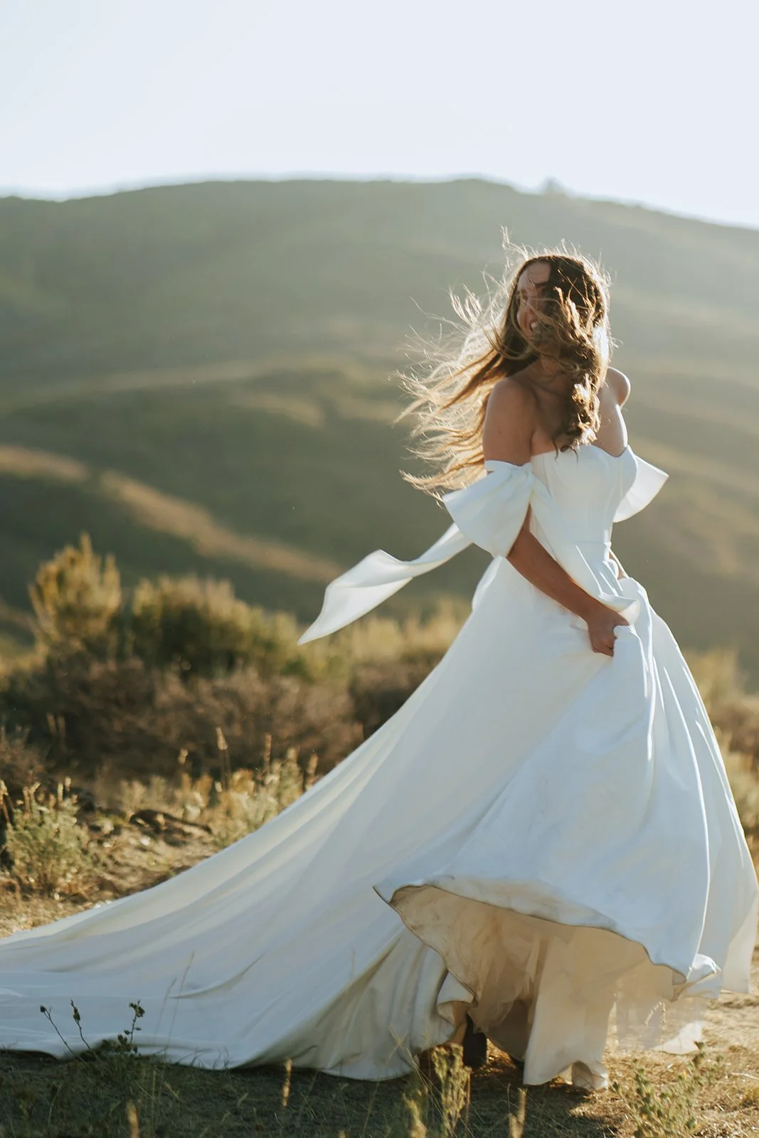 A bride in a flowing wedding dress runs playfully throughout a scenic mountain pass as the sun lights her from behind - photography by Poise and Ivy Imagery