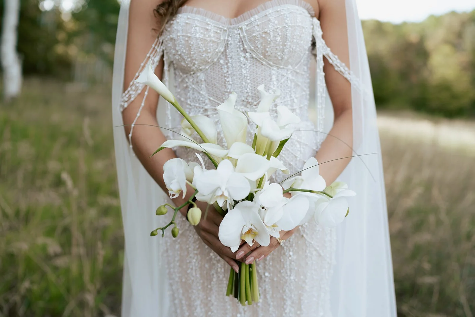 A bride in a beaded wedding gown holds a modern white bouquet - poise and ivy imagery