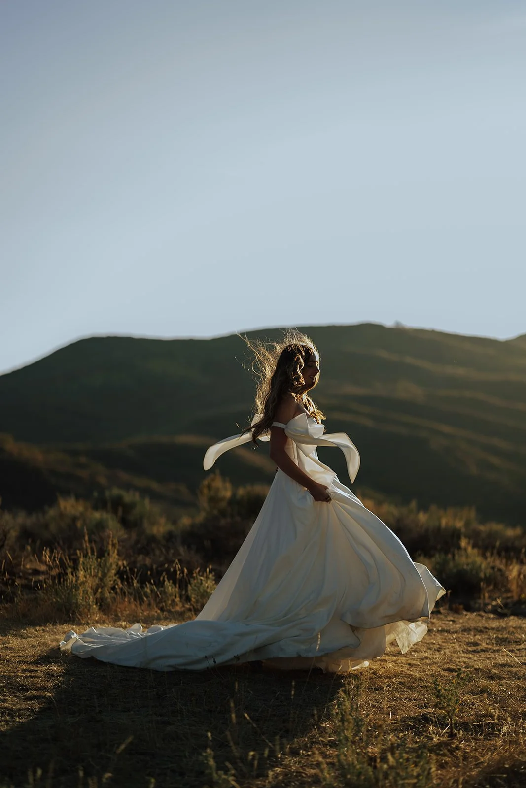 A bride in a wedding gown stands in a meadow with mountain peaks behind them - photography by Poise and Ivy Imagery