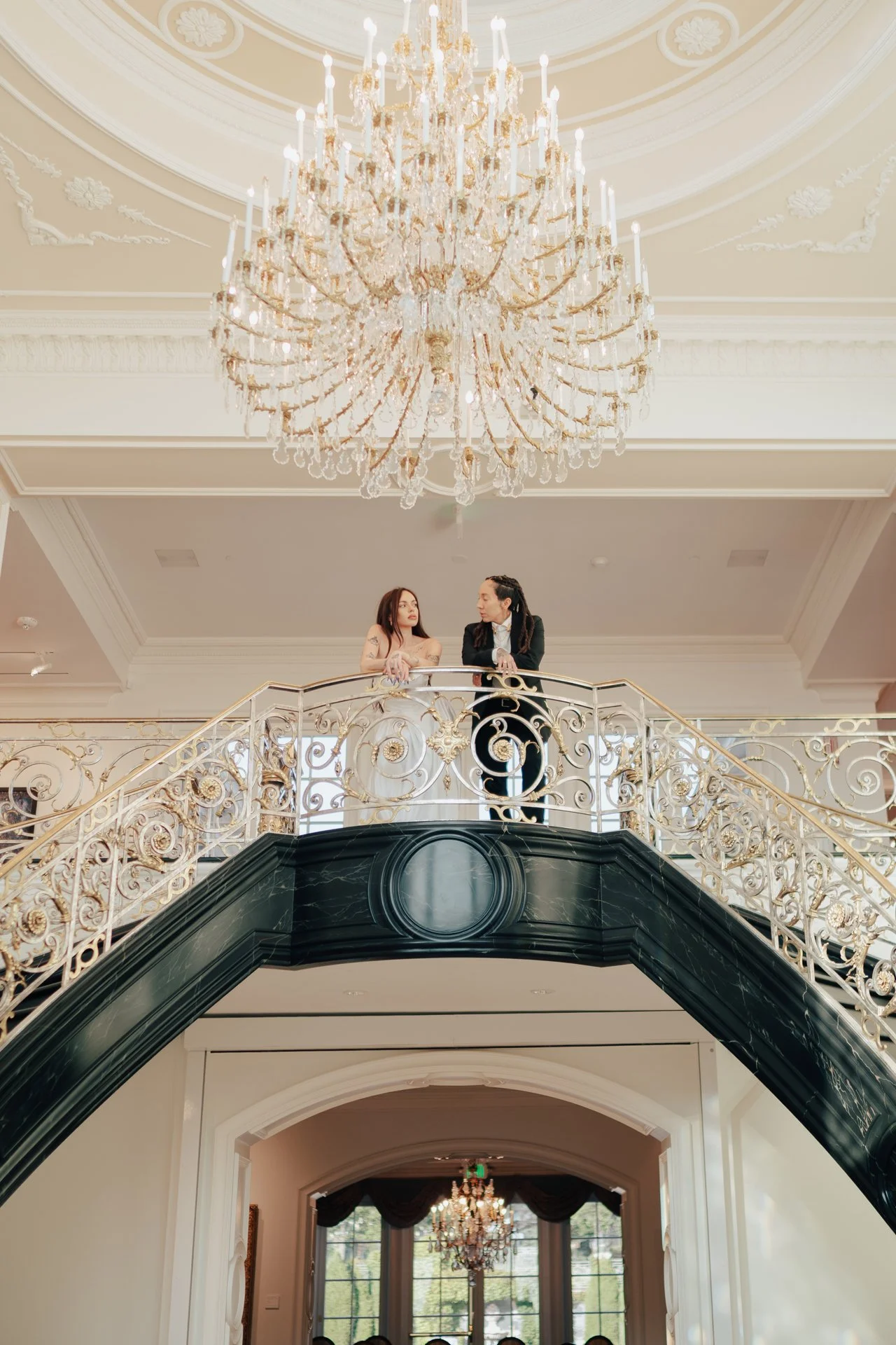 two brides embrace on an ornate double staircase - poise and ivy imagery