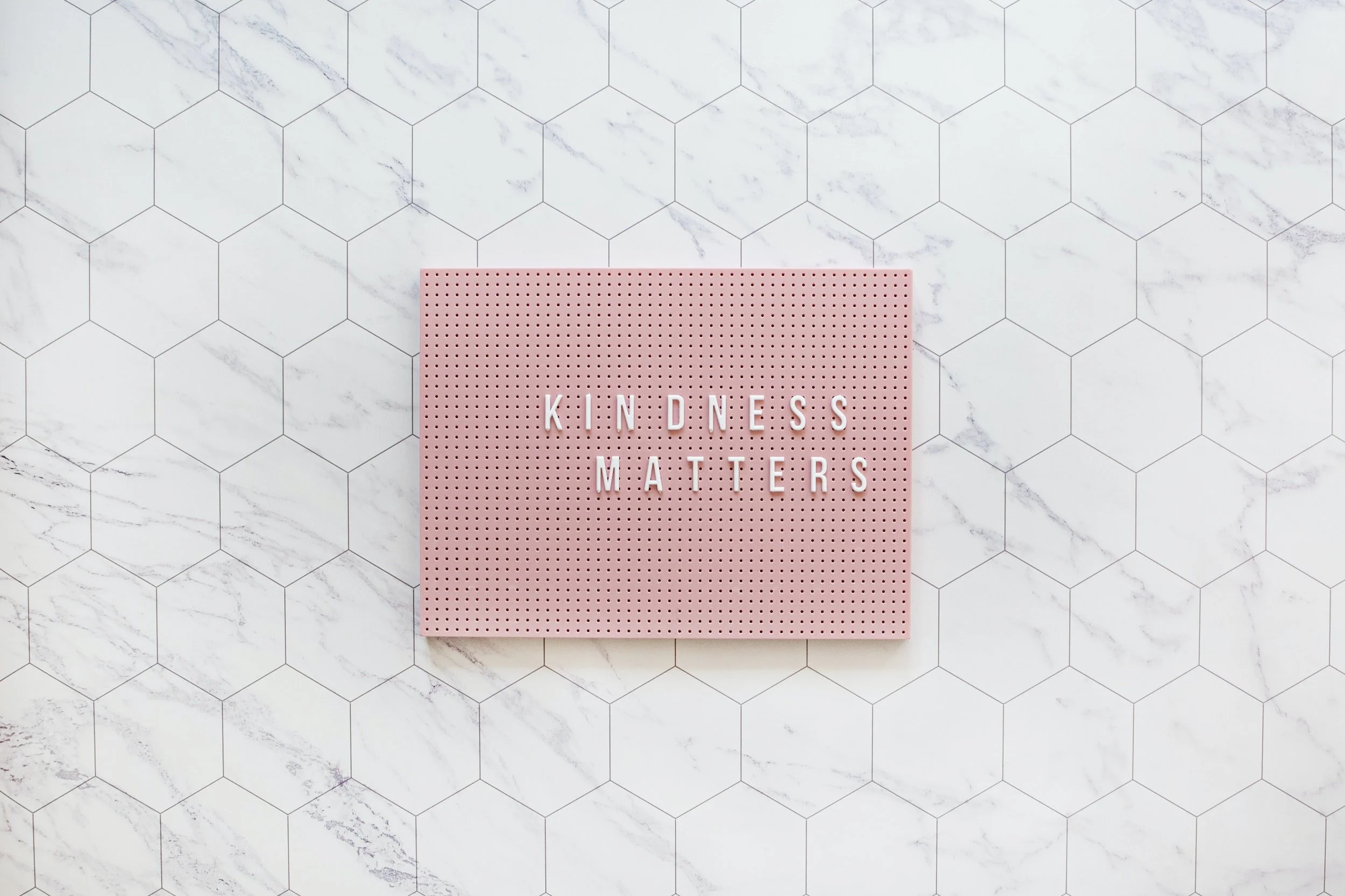 Pink letter board on white marble tile floor displaying the message 'Kindness Matters'.