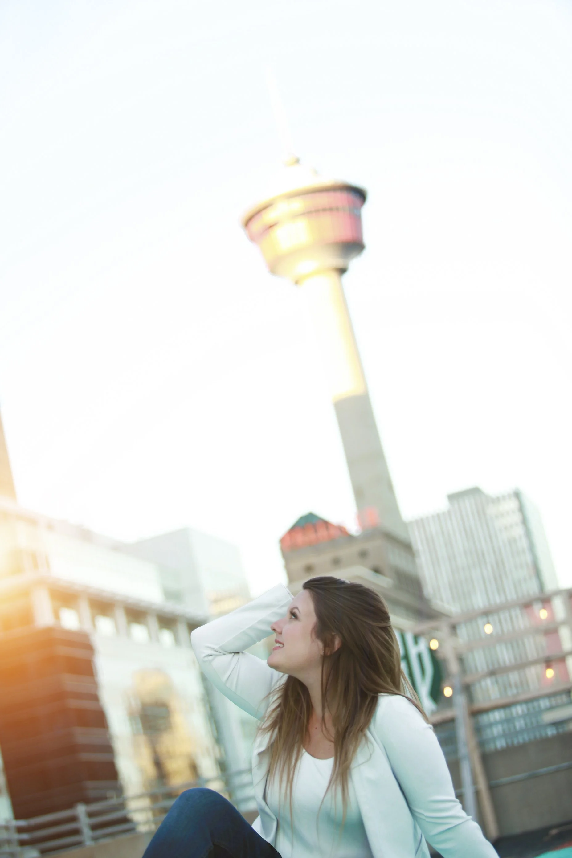 A young woman looks up at the calgary tower in the distance.