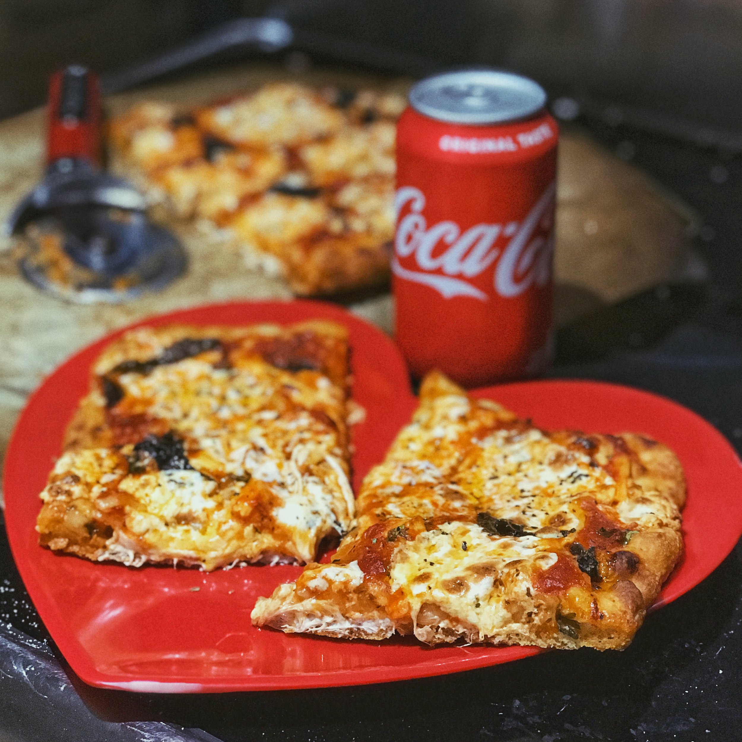 Homemade and handcrafted pizza on a red heart shaped plate with a red pizza knife and red coca cola can in the background. Pizza handmade by Ellen Avigliano. Styled and shot by Ellen Avigliano.