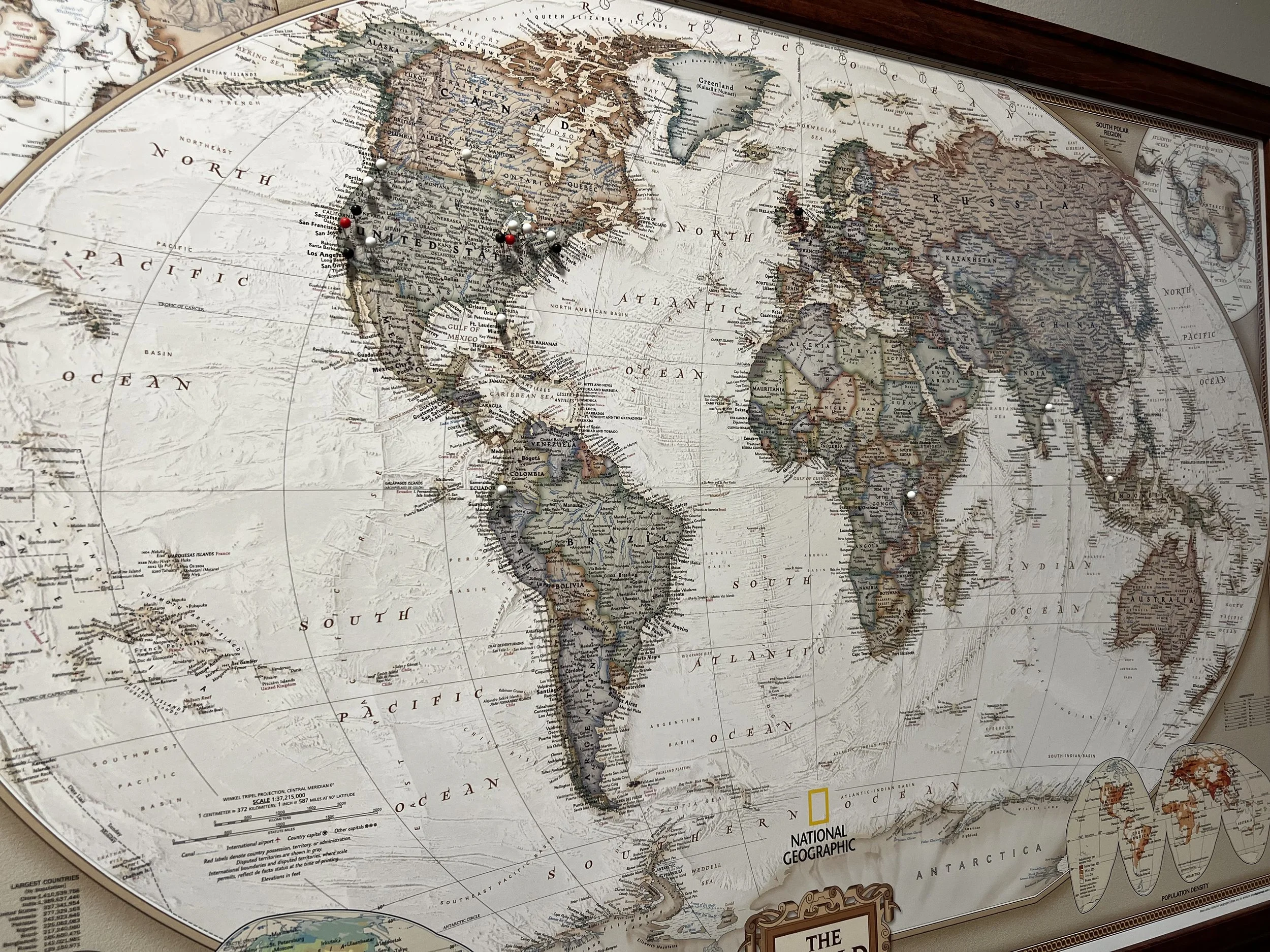 World map on a flat surface with some pins marking locations, featuring continents, countries, and oceans labeled, with a National Geographic logo visible.