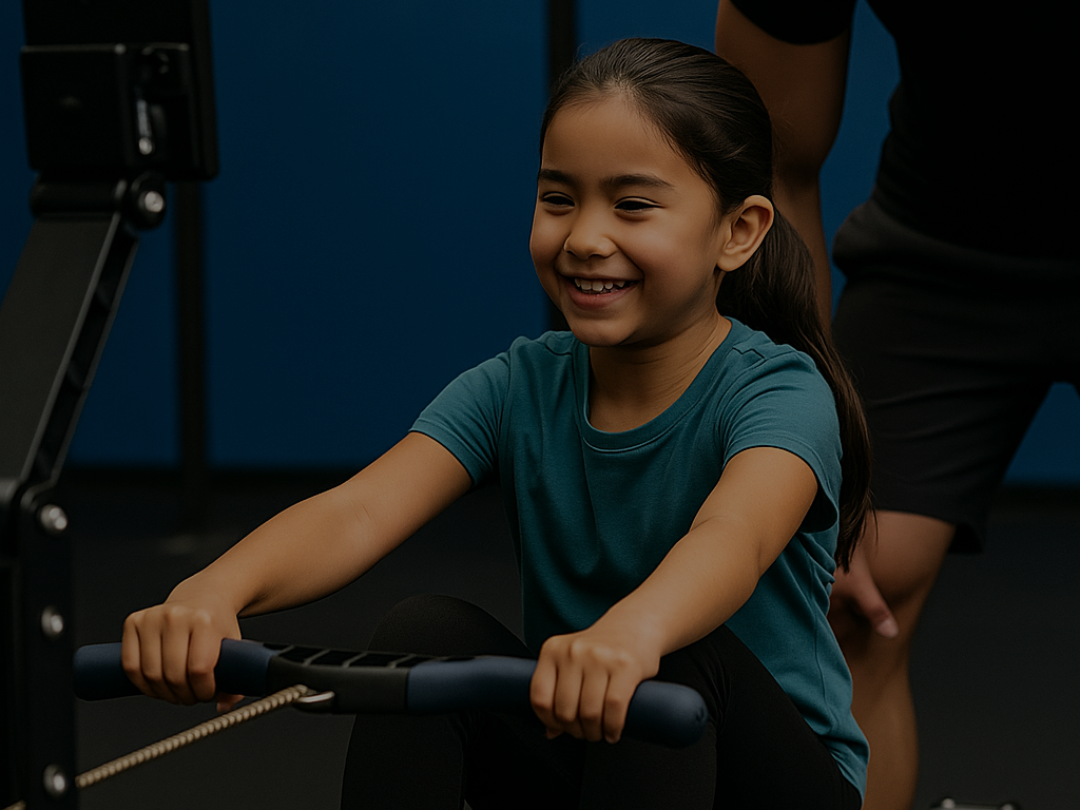 Smiling young girl using a rowing machine at CrossFit 1864 East London near Canary Wharf during a CrossFit Kids class.