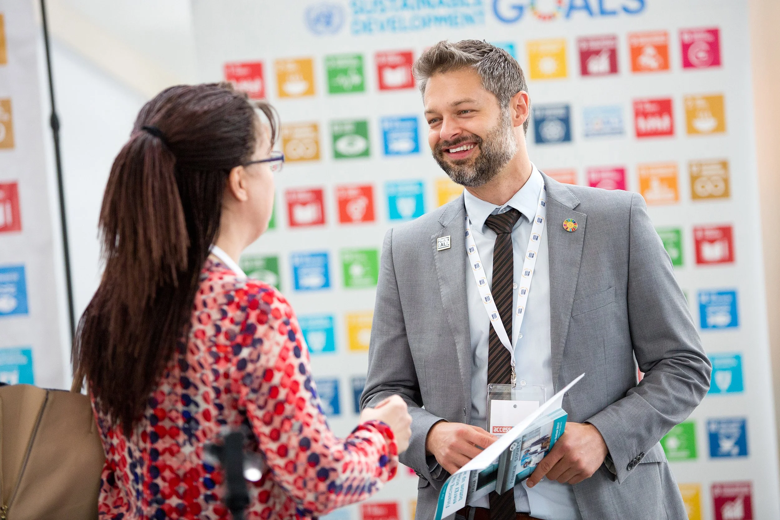 Man speaking to woman at event with branding in background
