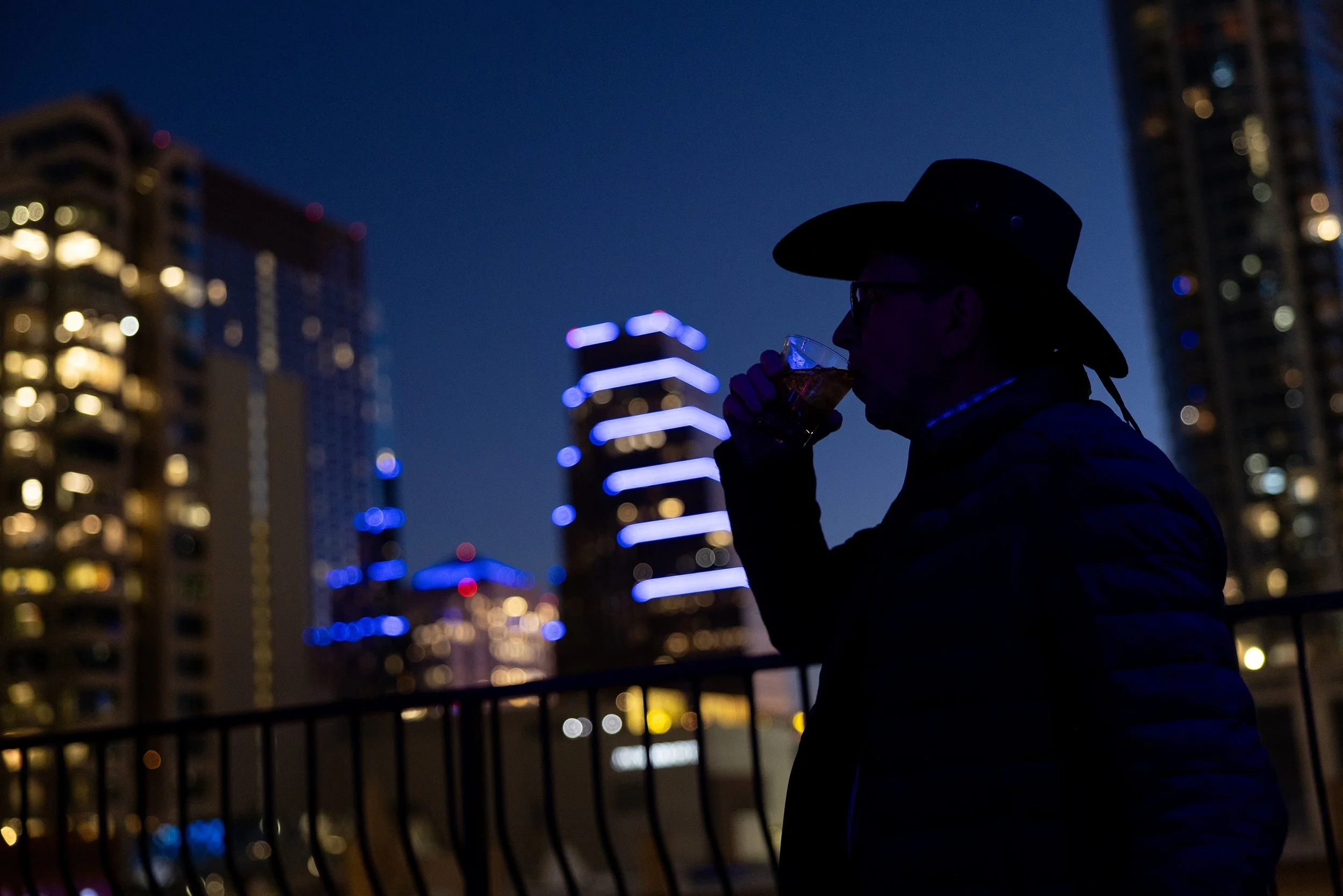 Silhouette of man in hat drinking against city