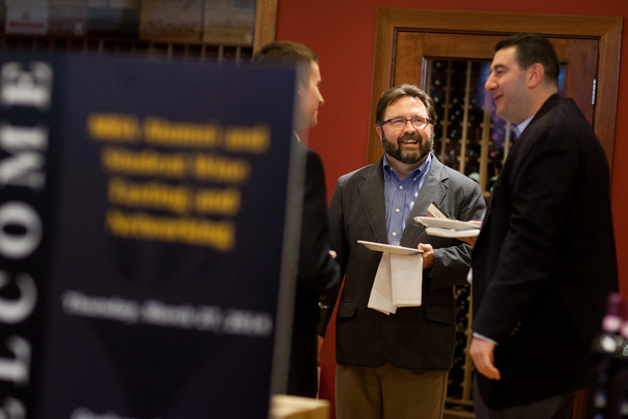 Group of 3 men speaking in back of branding sign