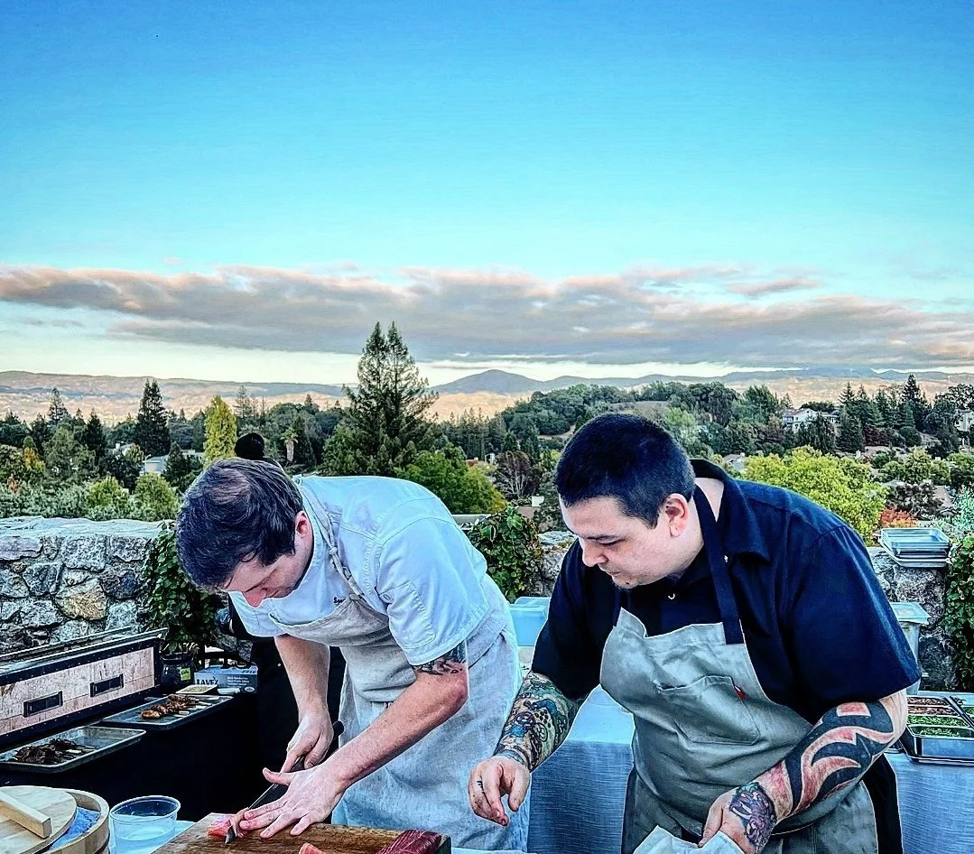 Chef Nate Maeda-Smouse is preparing omakase for our outdoor VIP event with a scenic view of trees, hills, and a cloudy sky.