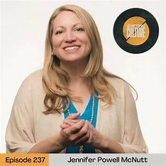 Smiling woman with blonde hair wearing a beige cardigan and blue blouse, standing in front of a white background. There is a circular logo behind her and an orange banner at the bottom with text.