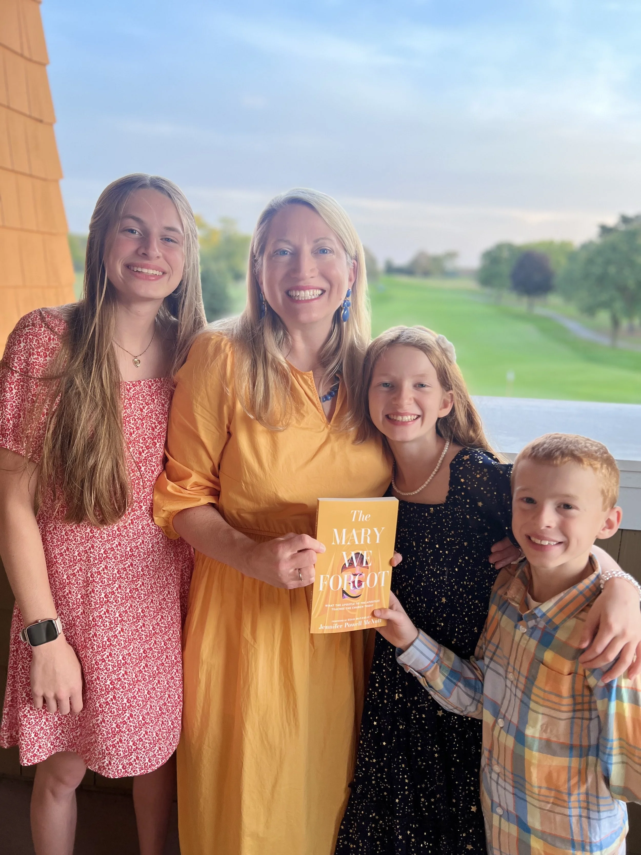Family gathered inside near a window with a view of the outdoors, holding a book titled 'The Mary We Forgot'.