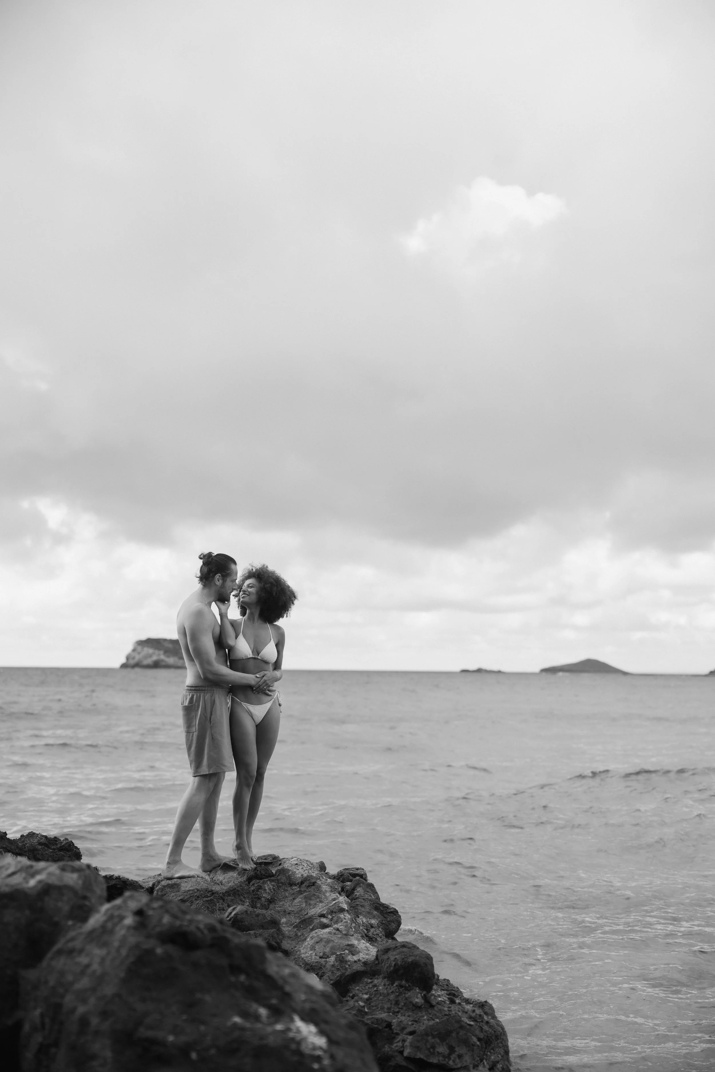 Couple smiling on seaside rocks in casual attire on Ibiza beach