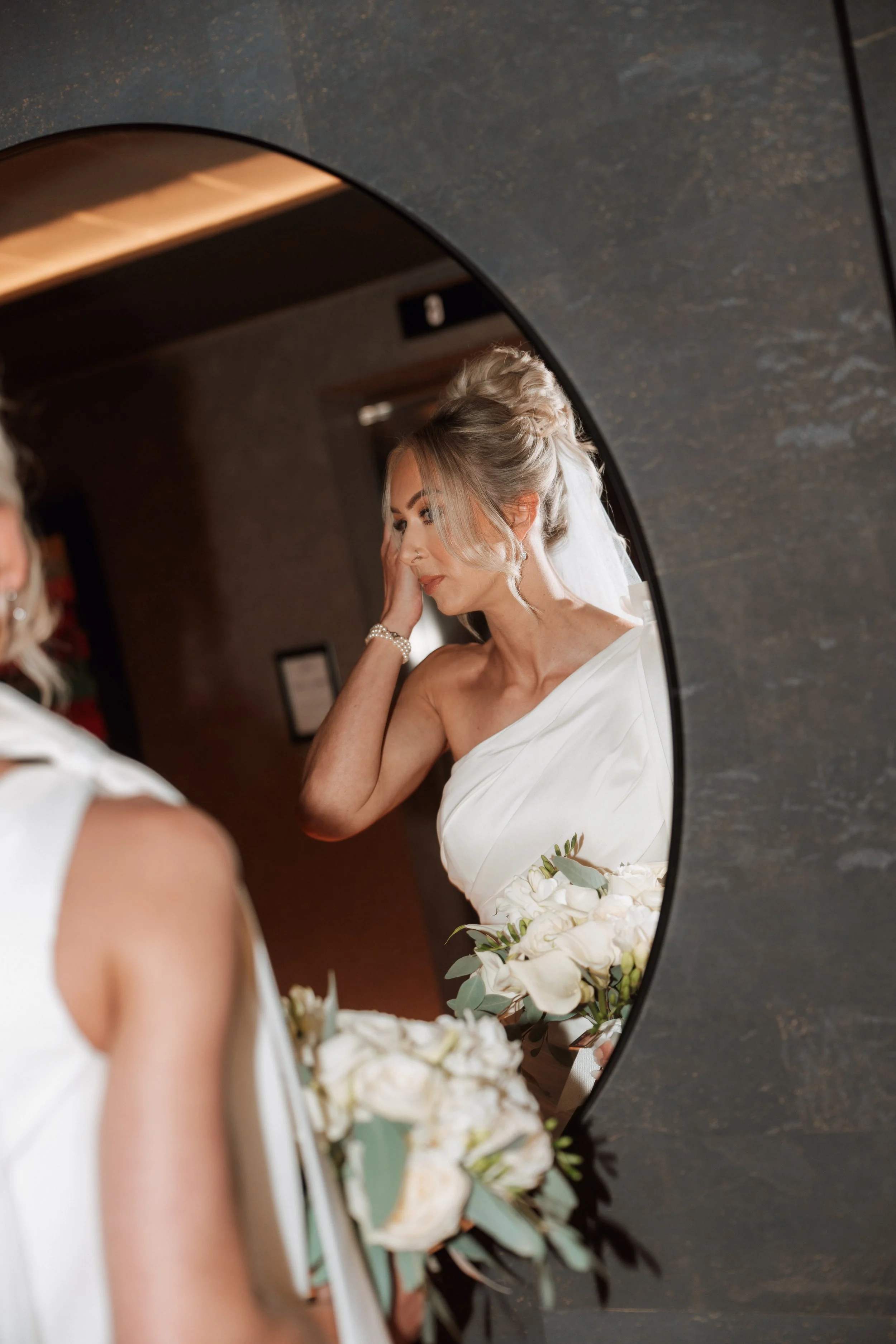 Bride looking in mirror holding white bouquet on wedding morning 