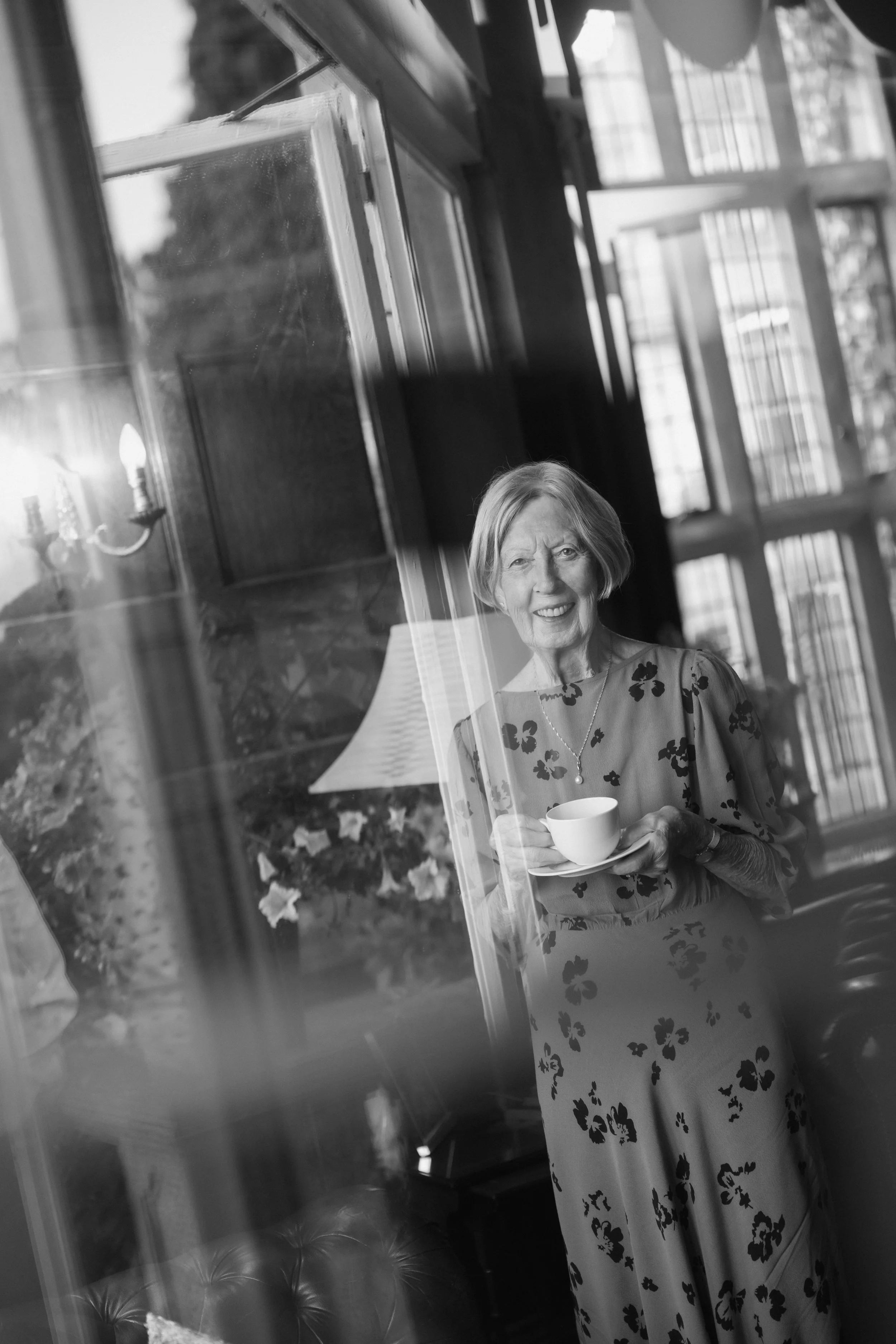 Elderly woman smiling indoors while holding teacup and saucer at Goldsborough hall 
