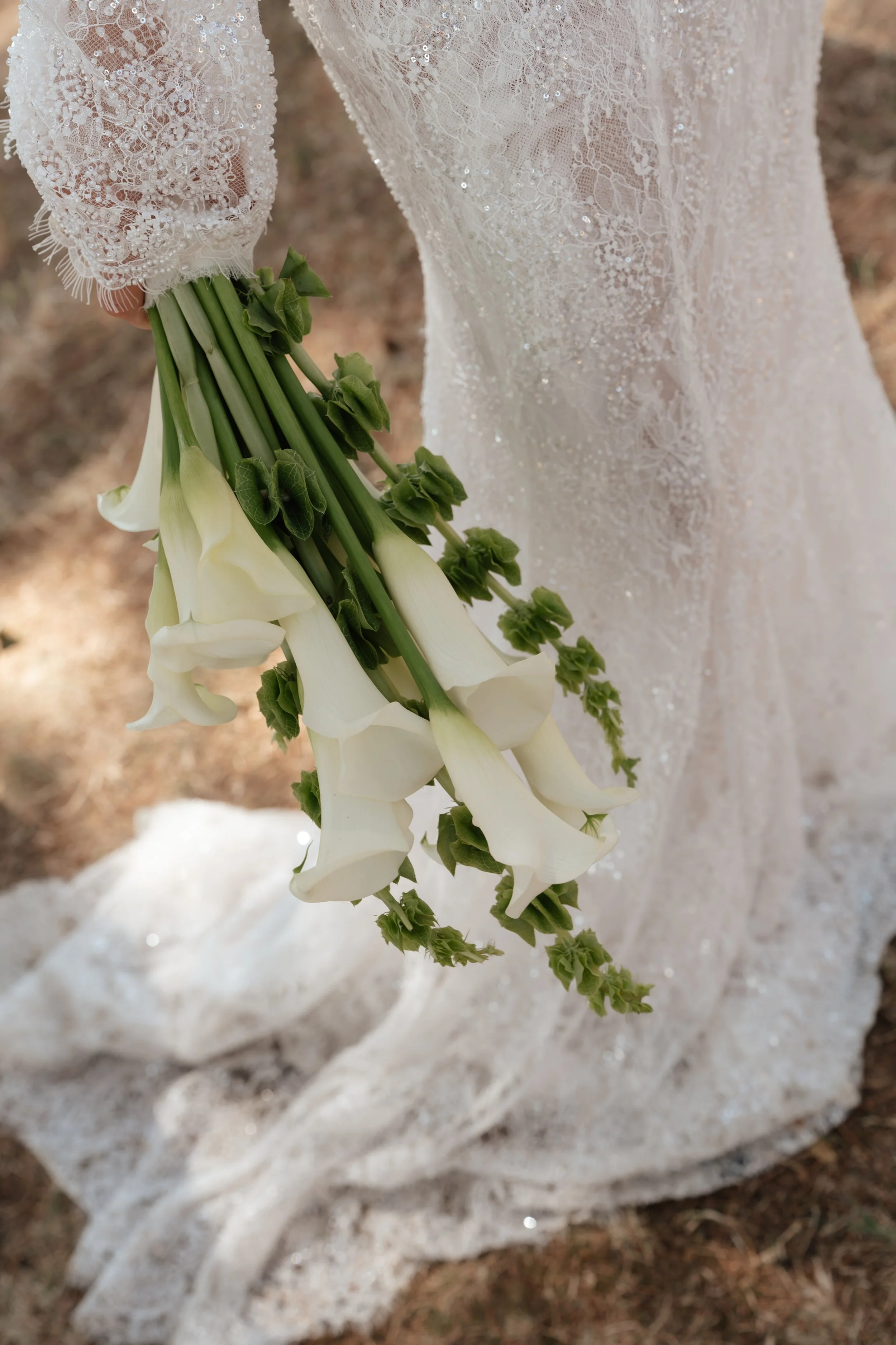 Bride holding white calla lily bouquet in lace gown during ceremony in Tuscany