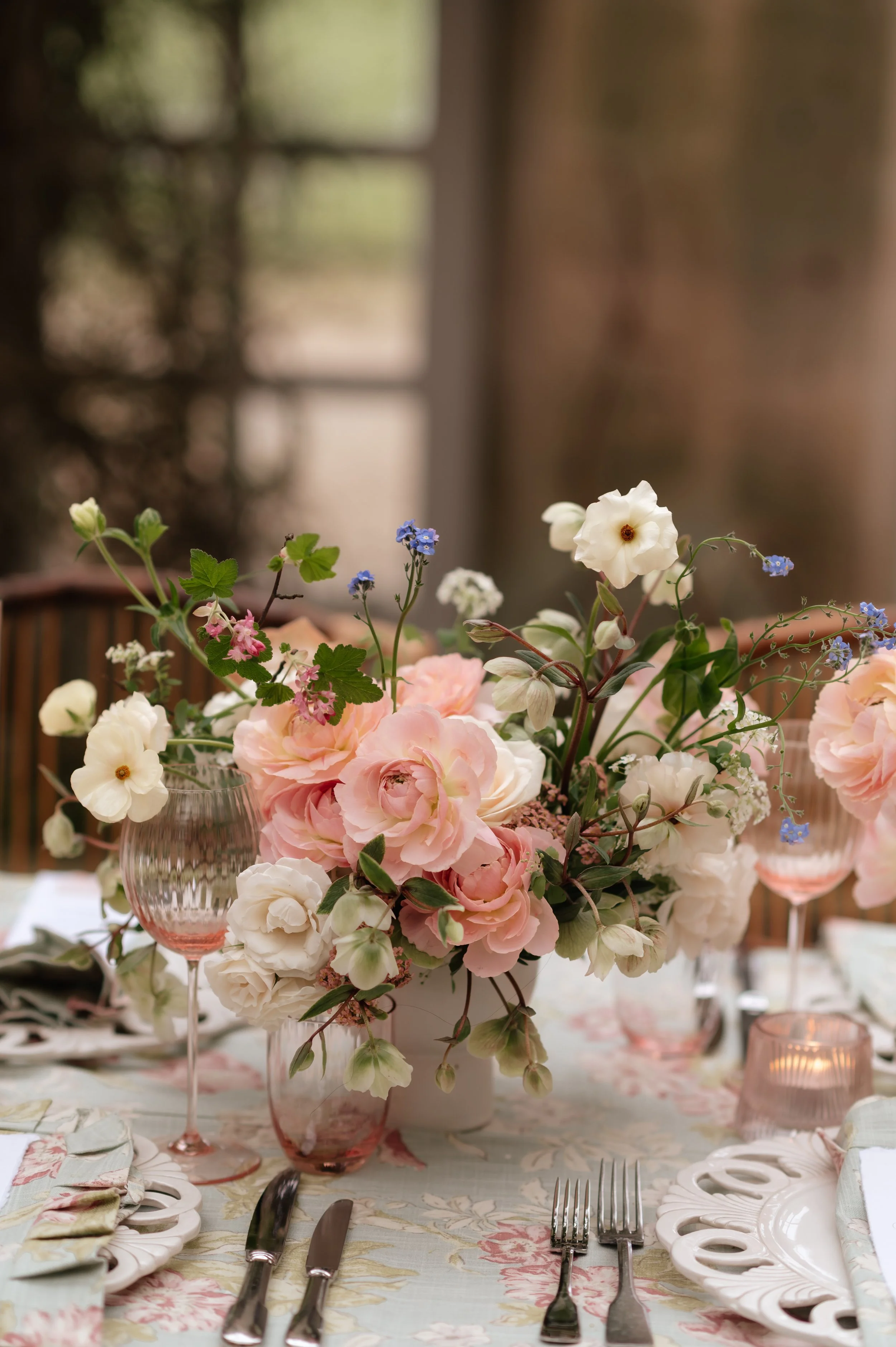 A floral centerpiece with pink and white flowers on a dining table with glassware, utensils, and decorative plates at Harlaxton Manor
