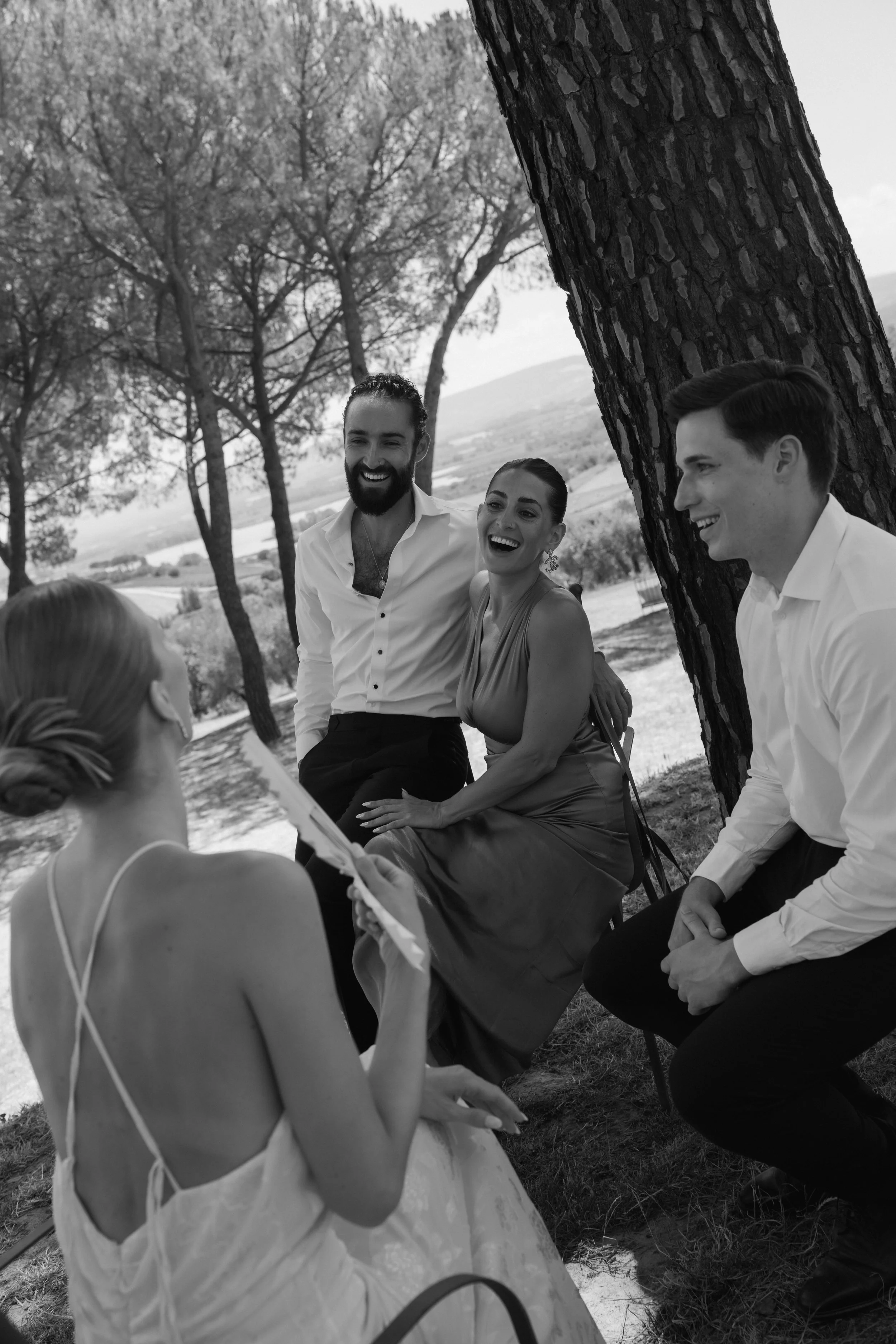 A group of five people enjoying a conversation outdoors under a tree, smiling and laughing, with scenic landscape in the background at Villa Cozzano