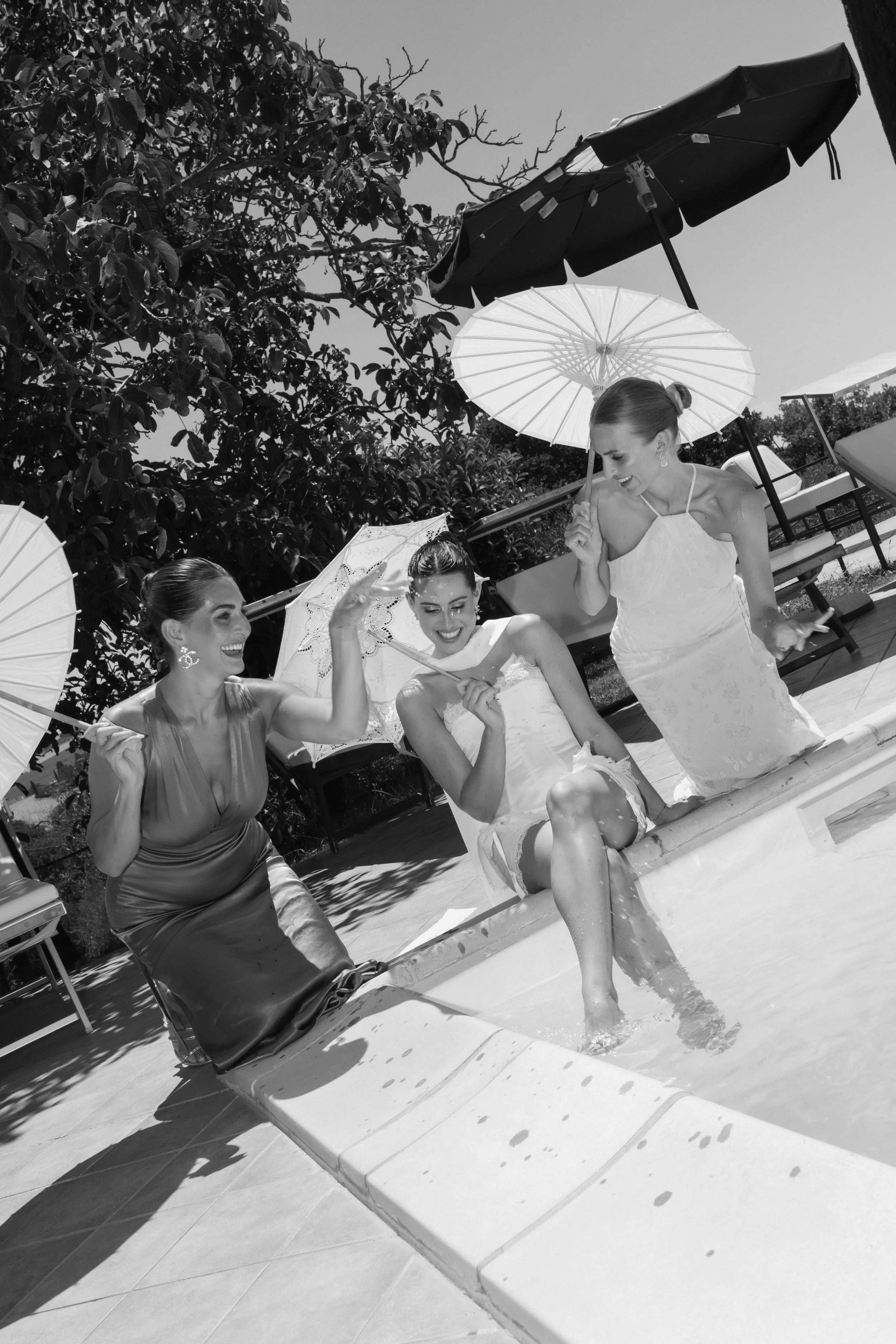 Three bridesmaids laughing near pool with parasols in Villa cozzano