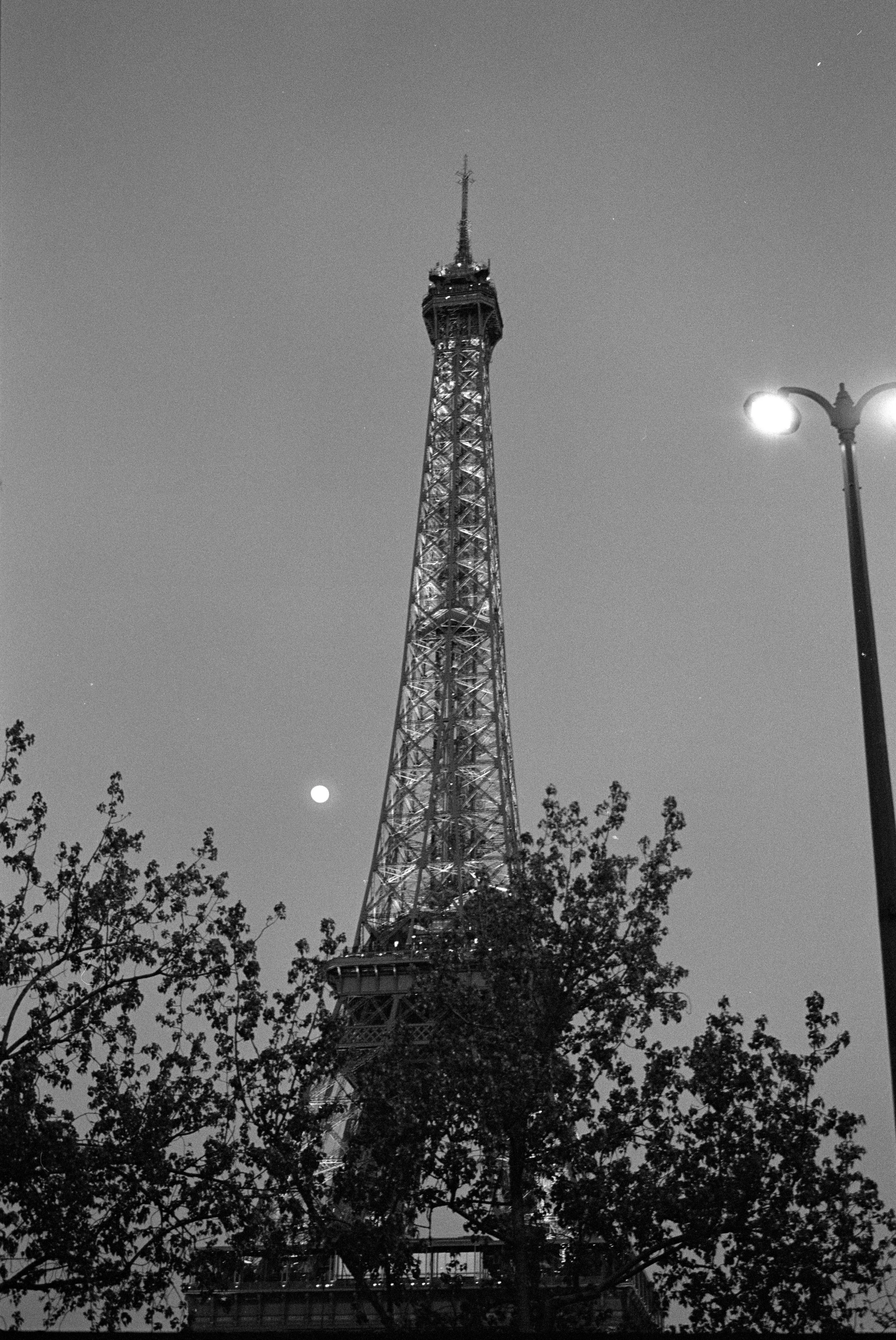 Black and white night view of Eiffel Tower in Paris with moon and illuminated street lamp