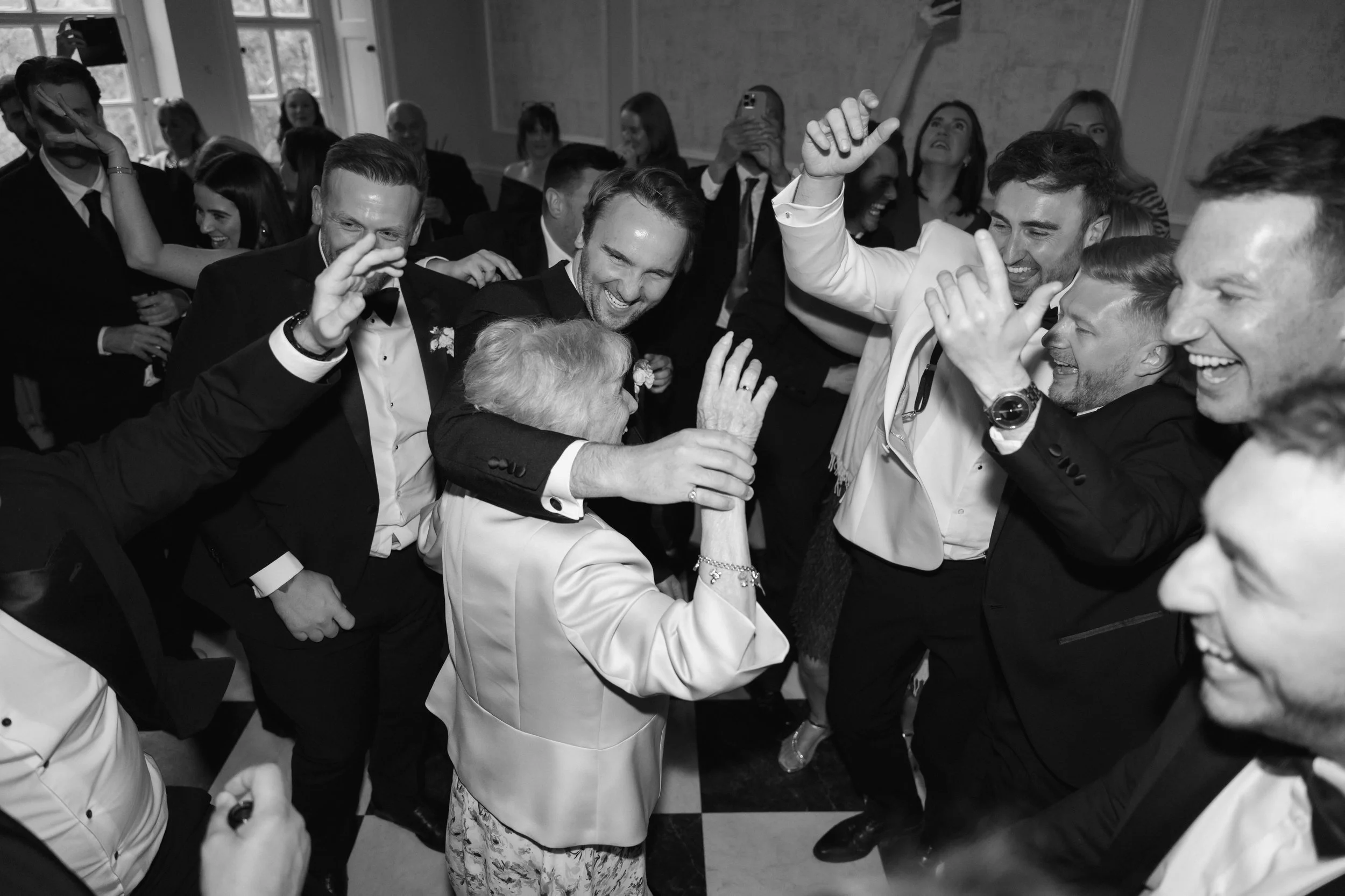 Group of wedding guests dancing and celebrating with elderly woman smiling at Howsham hall 