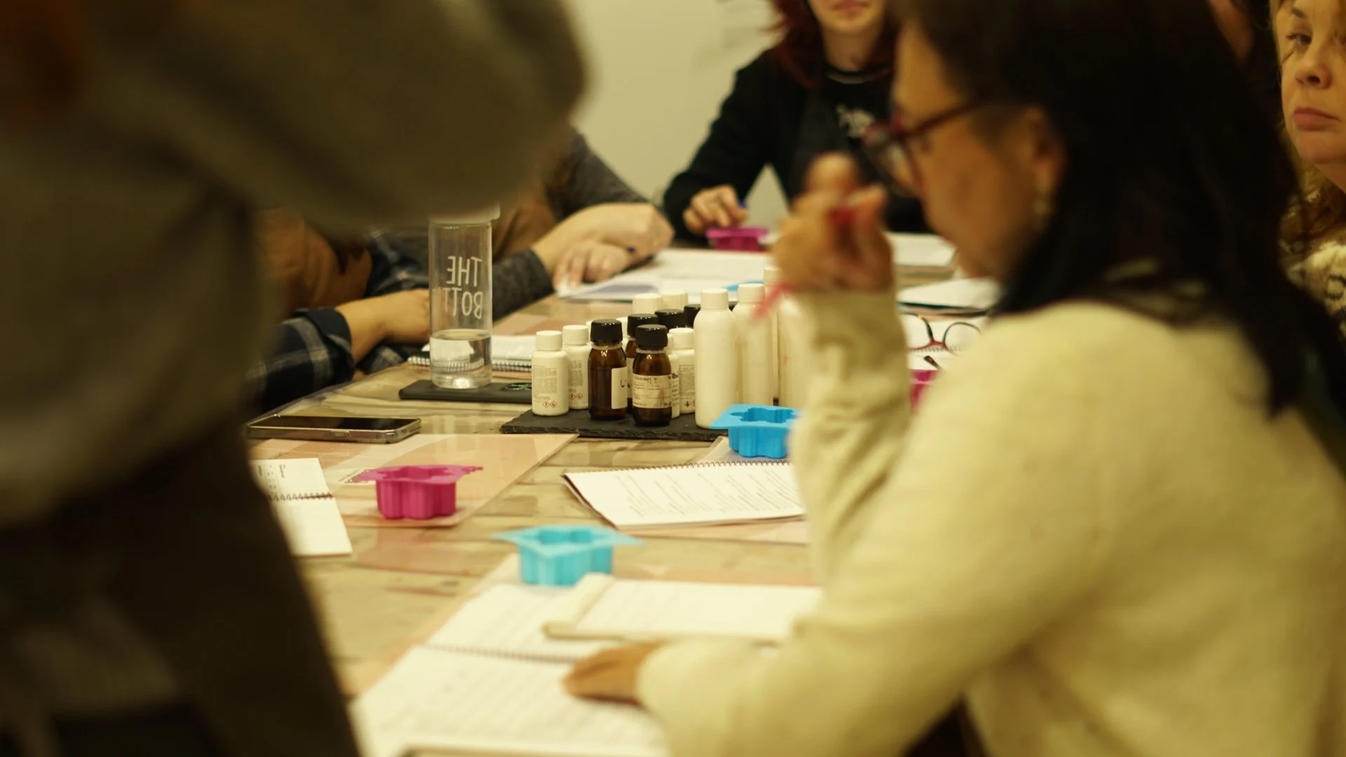 Grupo de personas en una reunión sentadas alrededor de una mesa con varios frascos y papeles.