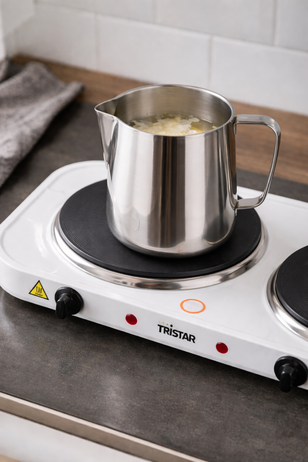 jarra de acero con cera derritiéndose sobre una placa de hornillo eléctrico ideal para hacer velas en casa