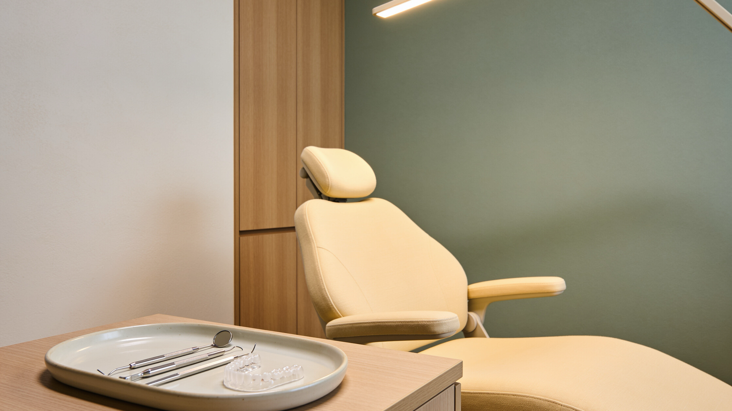 Calm Japandi style dental treatment room at Total Health Dental Care with a cream dental chair, sage green wall, and dental instruments on a ceramic tray