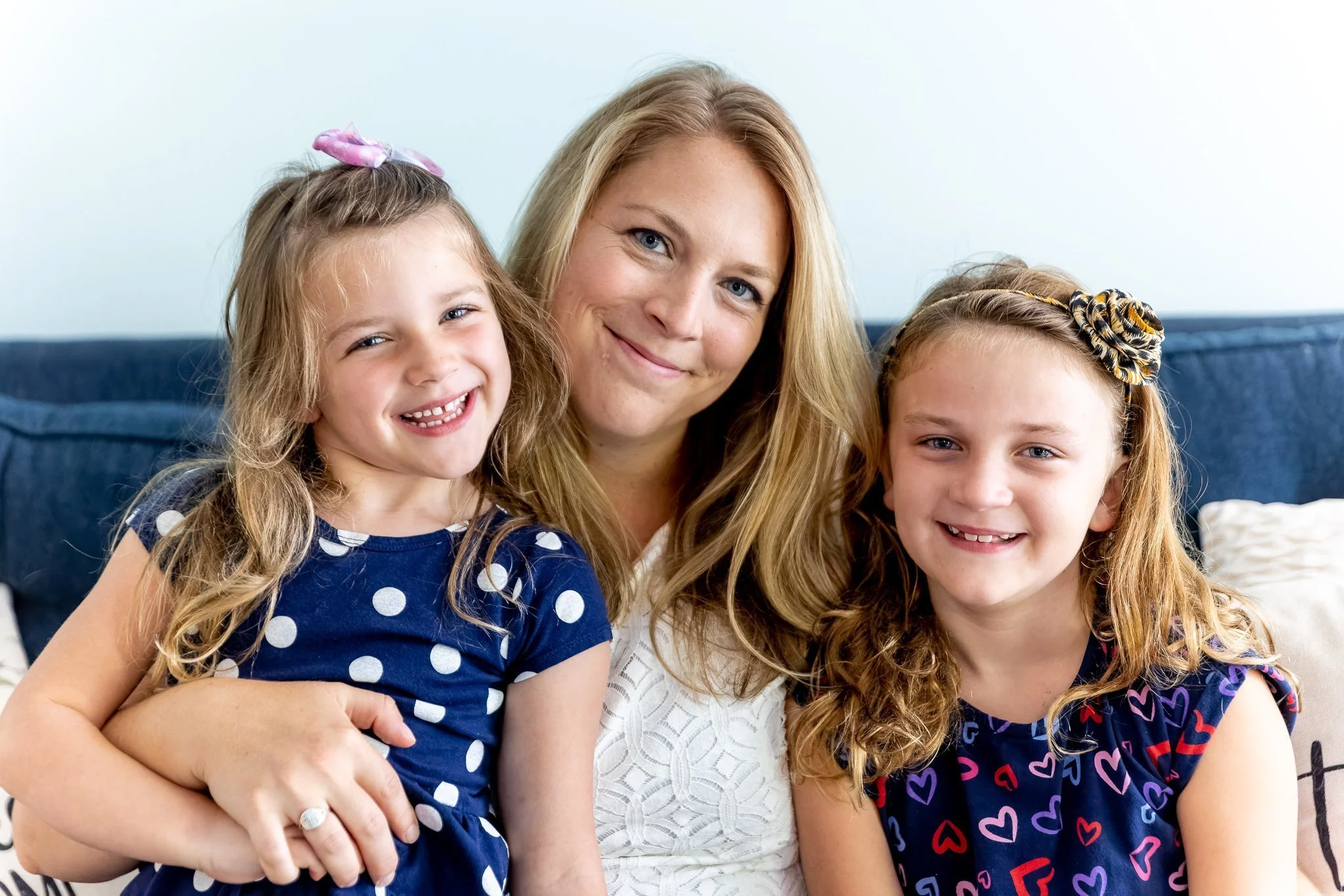 A woman with two young girls sitting on a blue couch, all smiling at the camera.