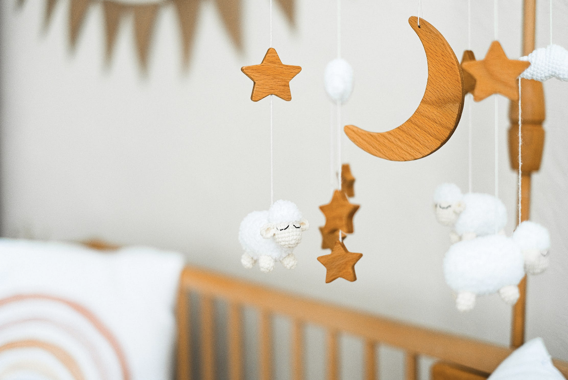 bright and light photo close up of a baby's mobile above a crib in a nursery, wood stars and moon, soft white sheep. Rainbow blanket in the background