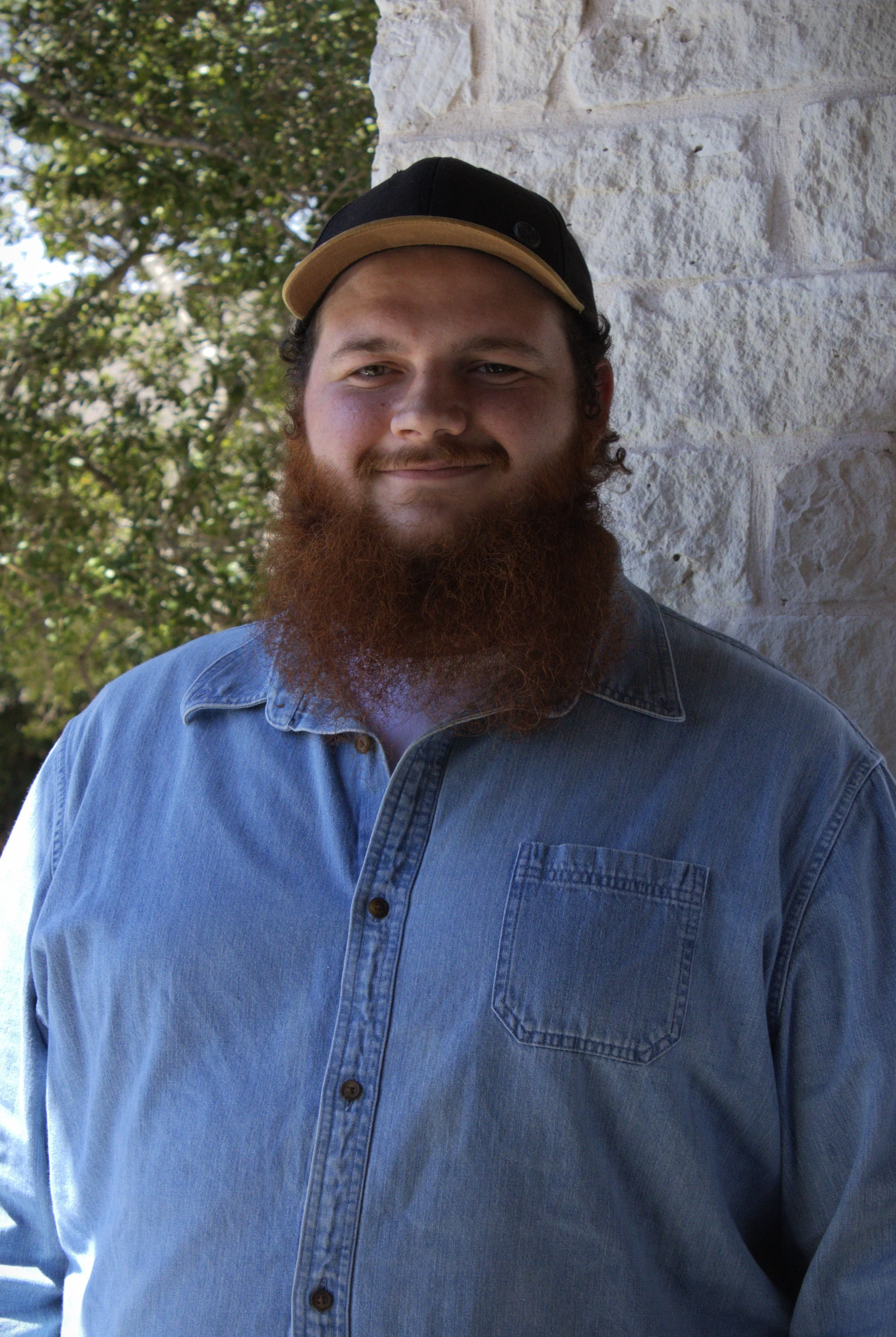 Hayden Bradshaw, TCC Irving Location supervisor and chess coach, smiling against a brick wall.