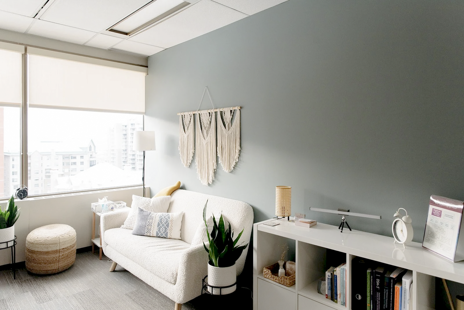 Bright living room with a large window, white sofa, plants, and decorative wall hanging