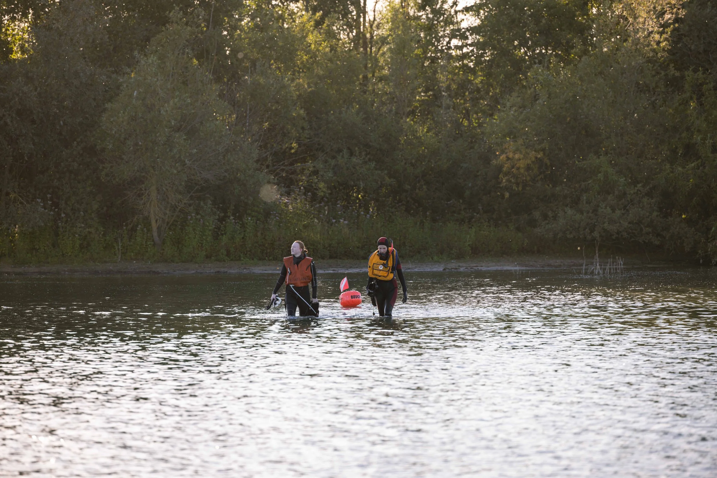 To redningsfolk går gennem vand med redningsudstyr mod en skov på kysten.