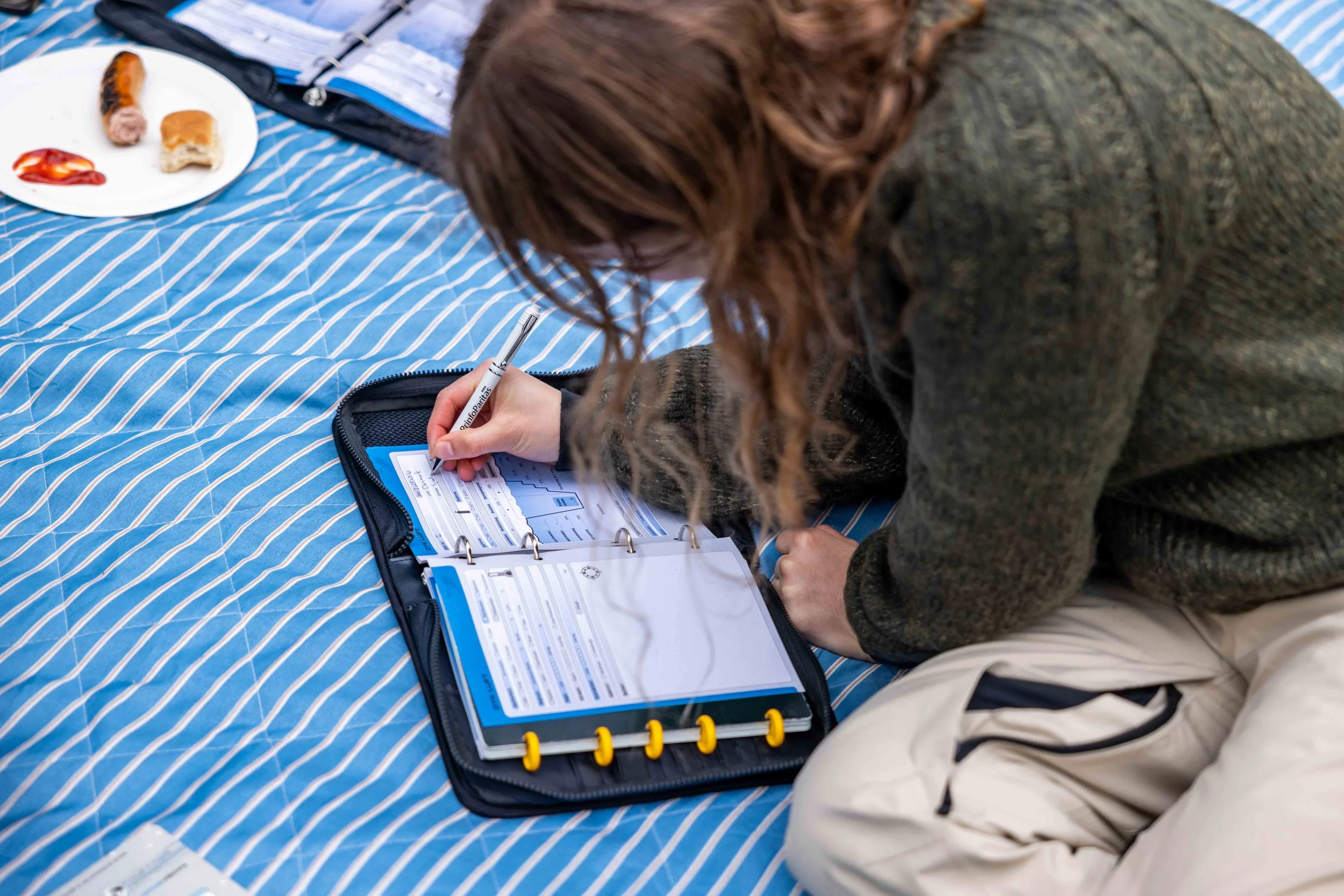 Person på knæ på et tæppe, der skriver i en mappe med formularer. Der er en tallerken med mad i baggrunden.