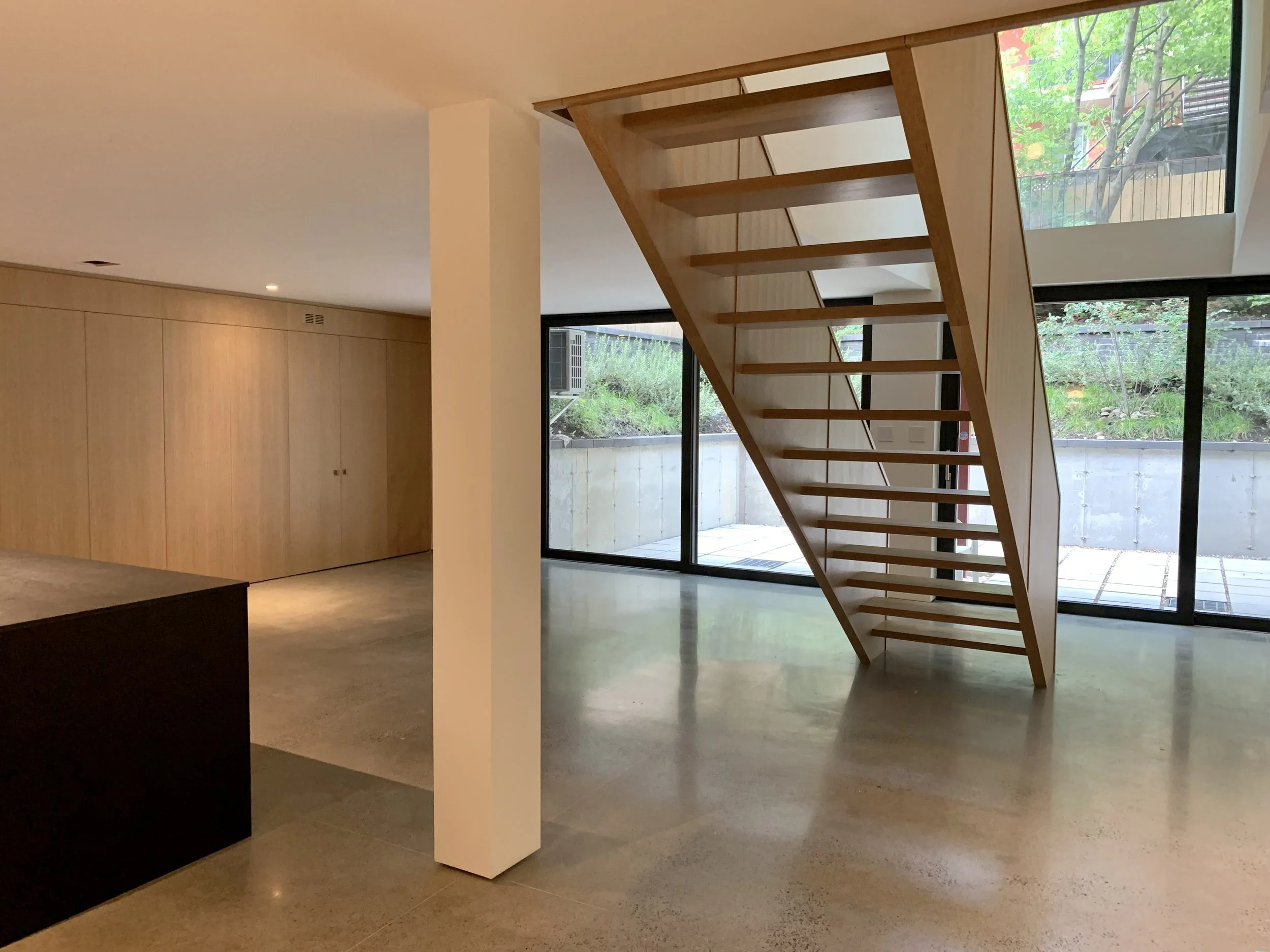 Modern interior with a wooden staircase, large floor-to-ceiling windows, and minimalistic design.