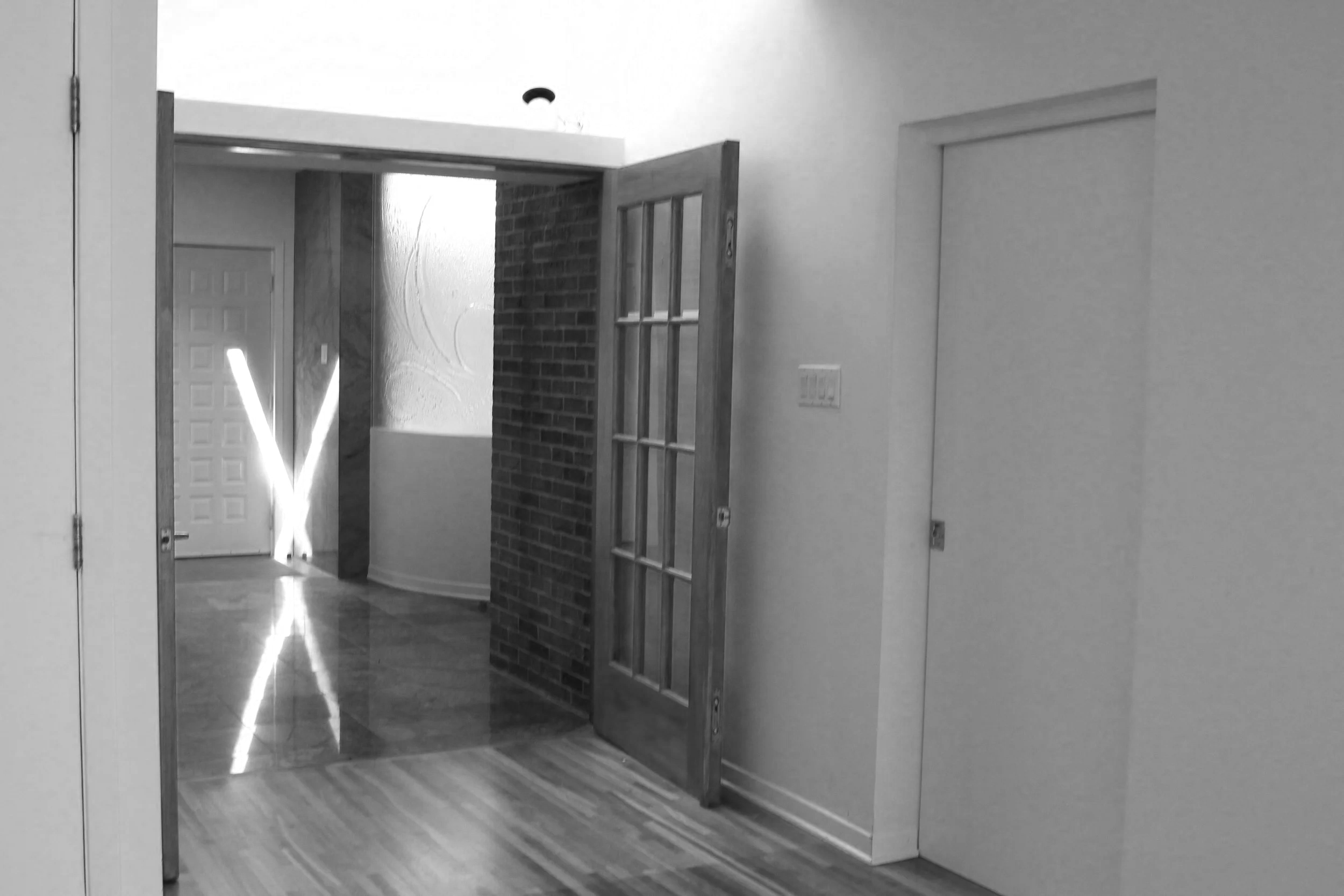 Interior view of a house with a doorway leading to a hallway, a glass-paned door, and a decorative corner with lighting, brick wall, and frosted window.