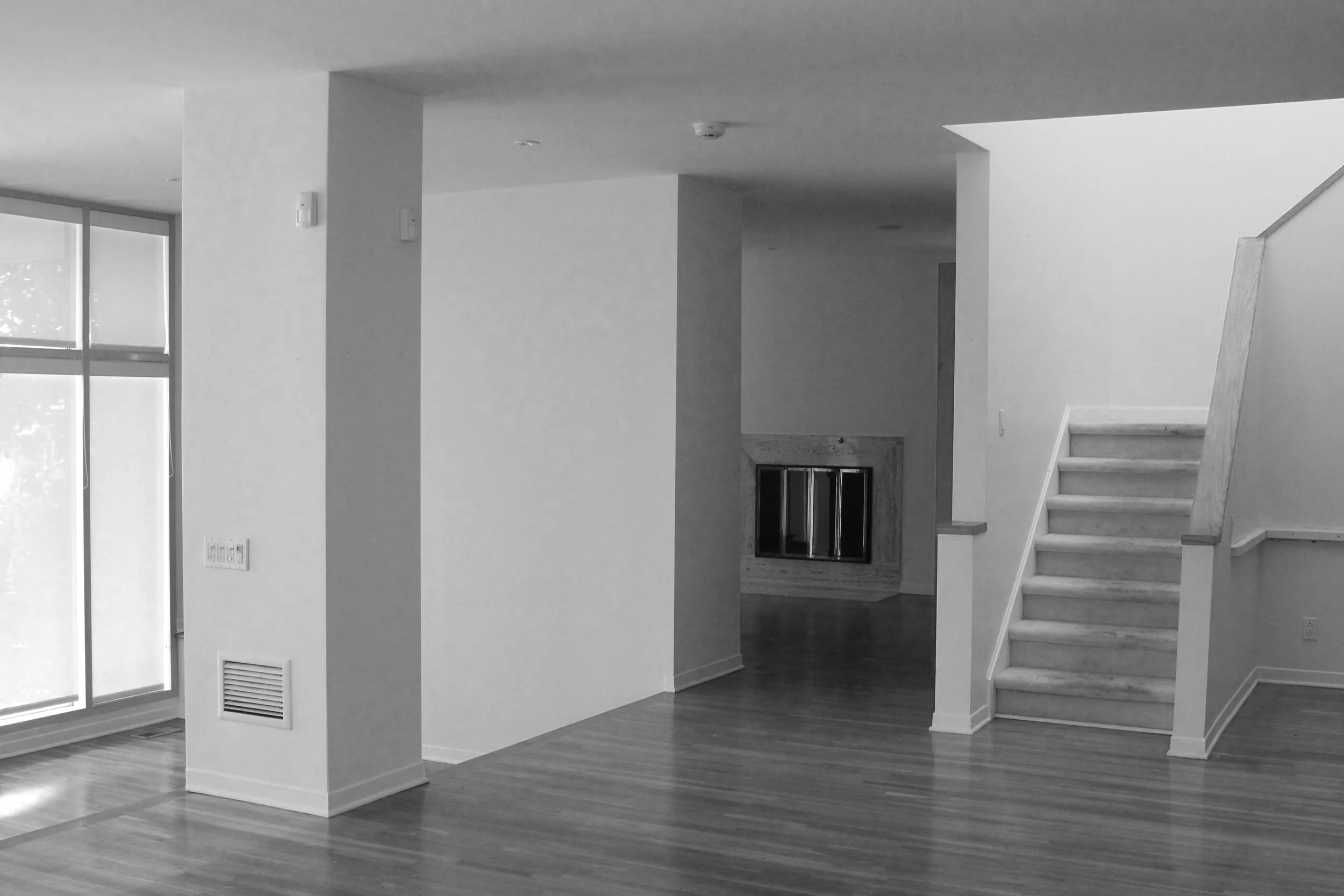 Interior of a modern house with a staircase, fireplace, large windows, and hardwood floors.