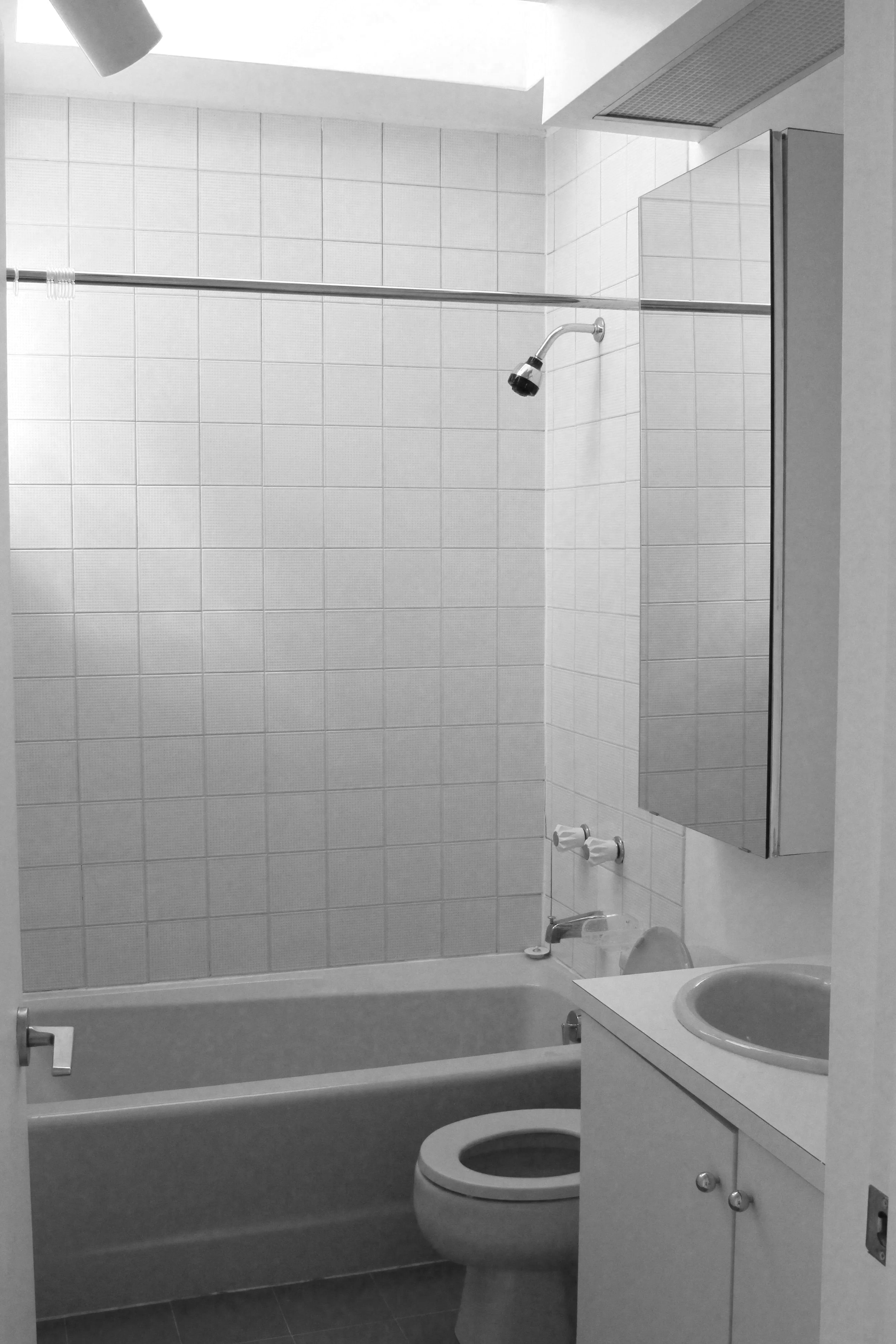 A bathroom with a bathtub, toilet, small sink, mirror, and tiled walls in black and white.