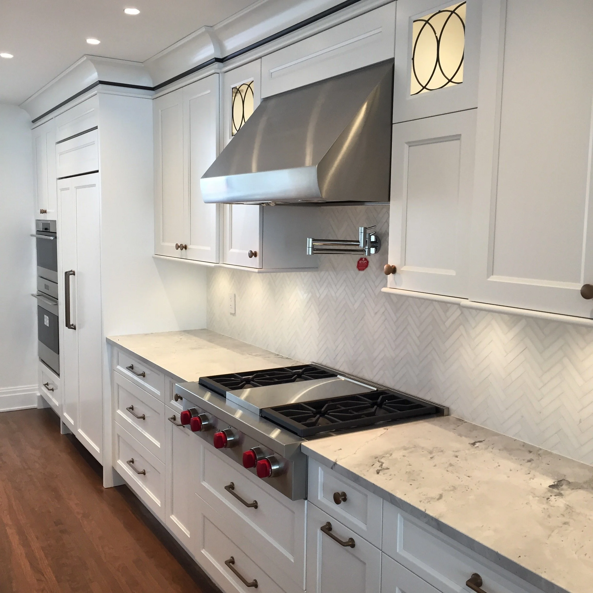 Modern kitchen with white cabinets, marble countertops, stainless steel stove with red knobs, and a stainless steel range hood.