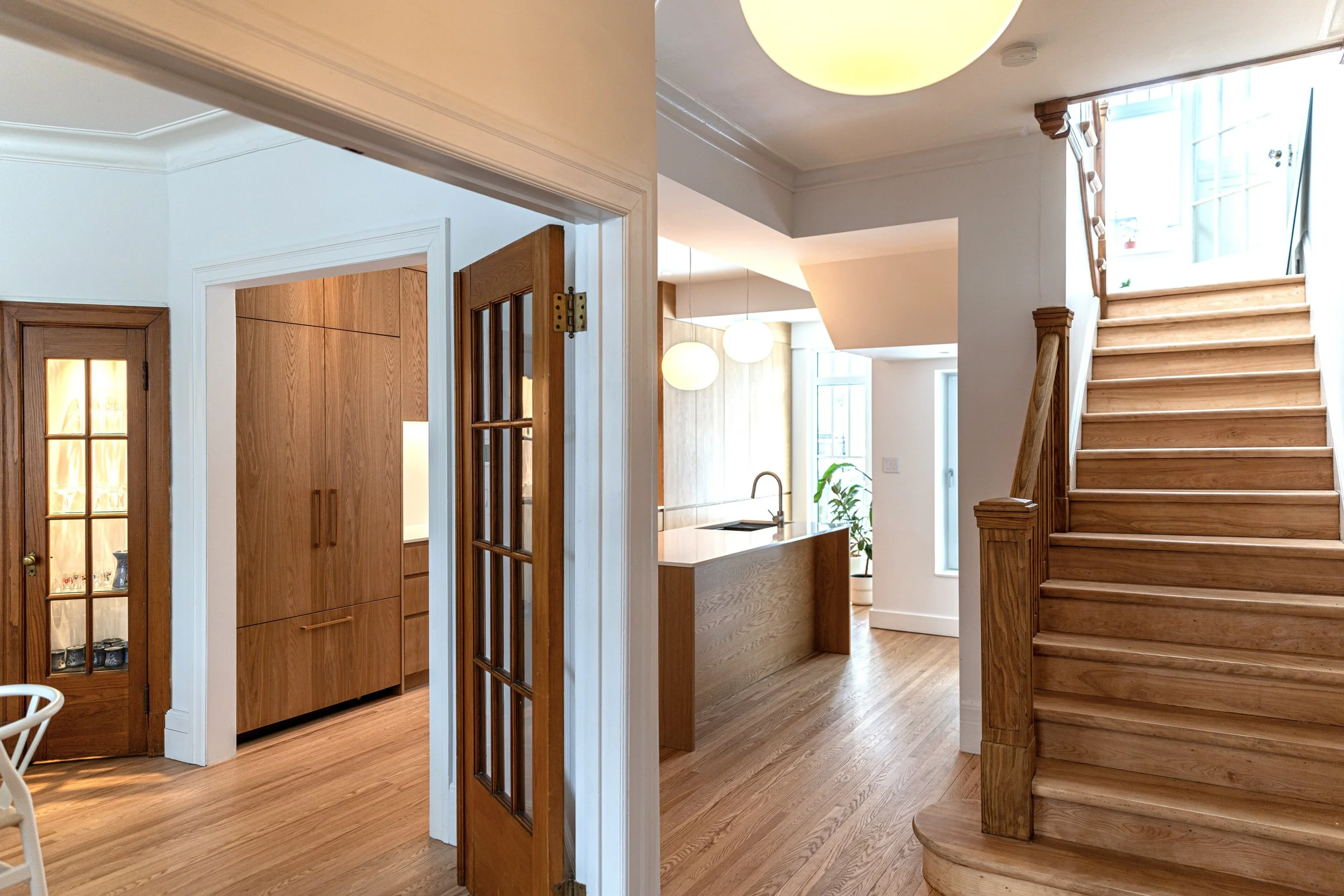 Interior of a home with wooden floors and staircase, kitchen with pendant lights, and a room with wooden cabinets.
