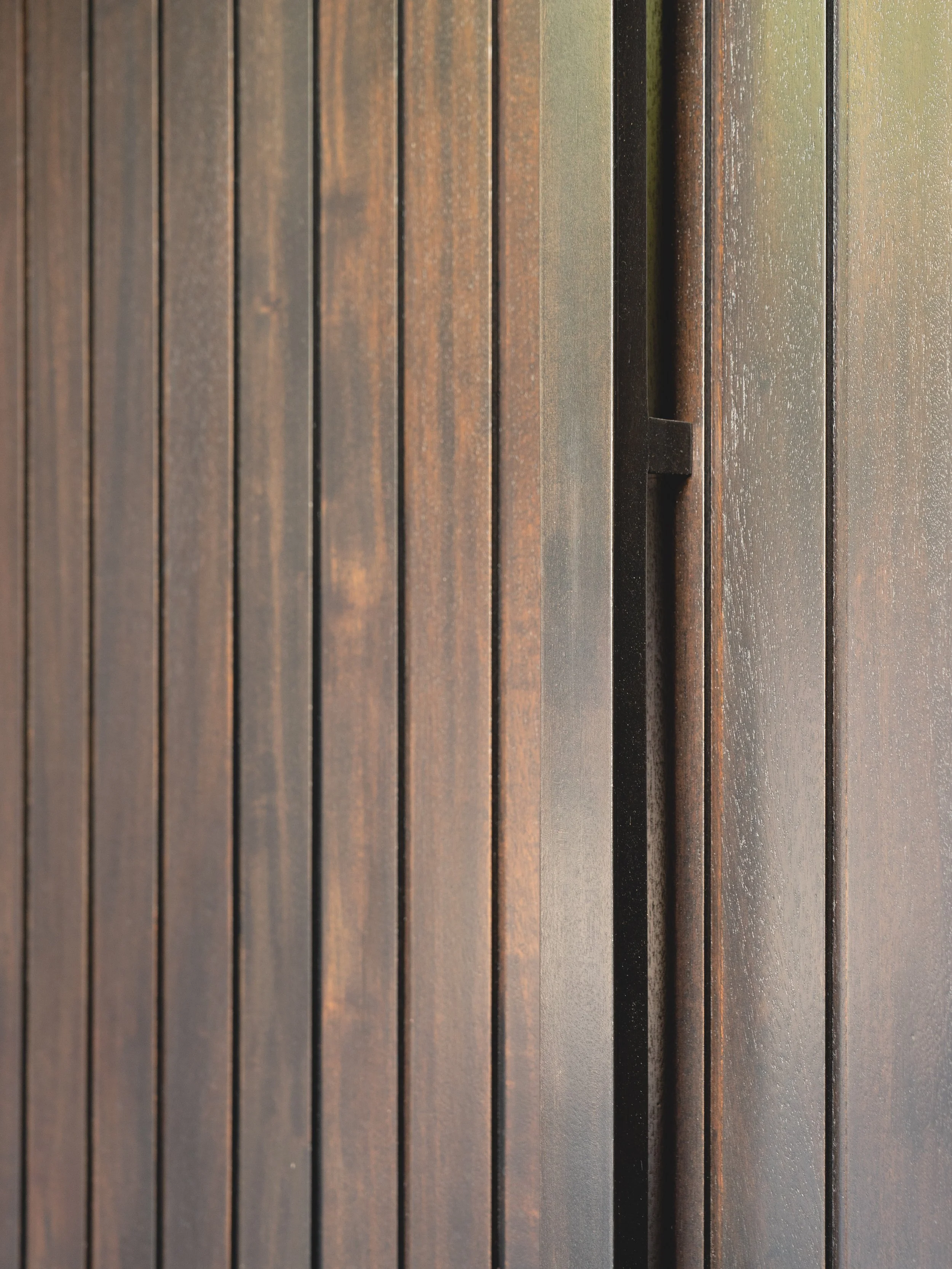 Close-up of a dark wooden door with vertical planks and a recessed handle.