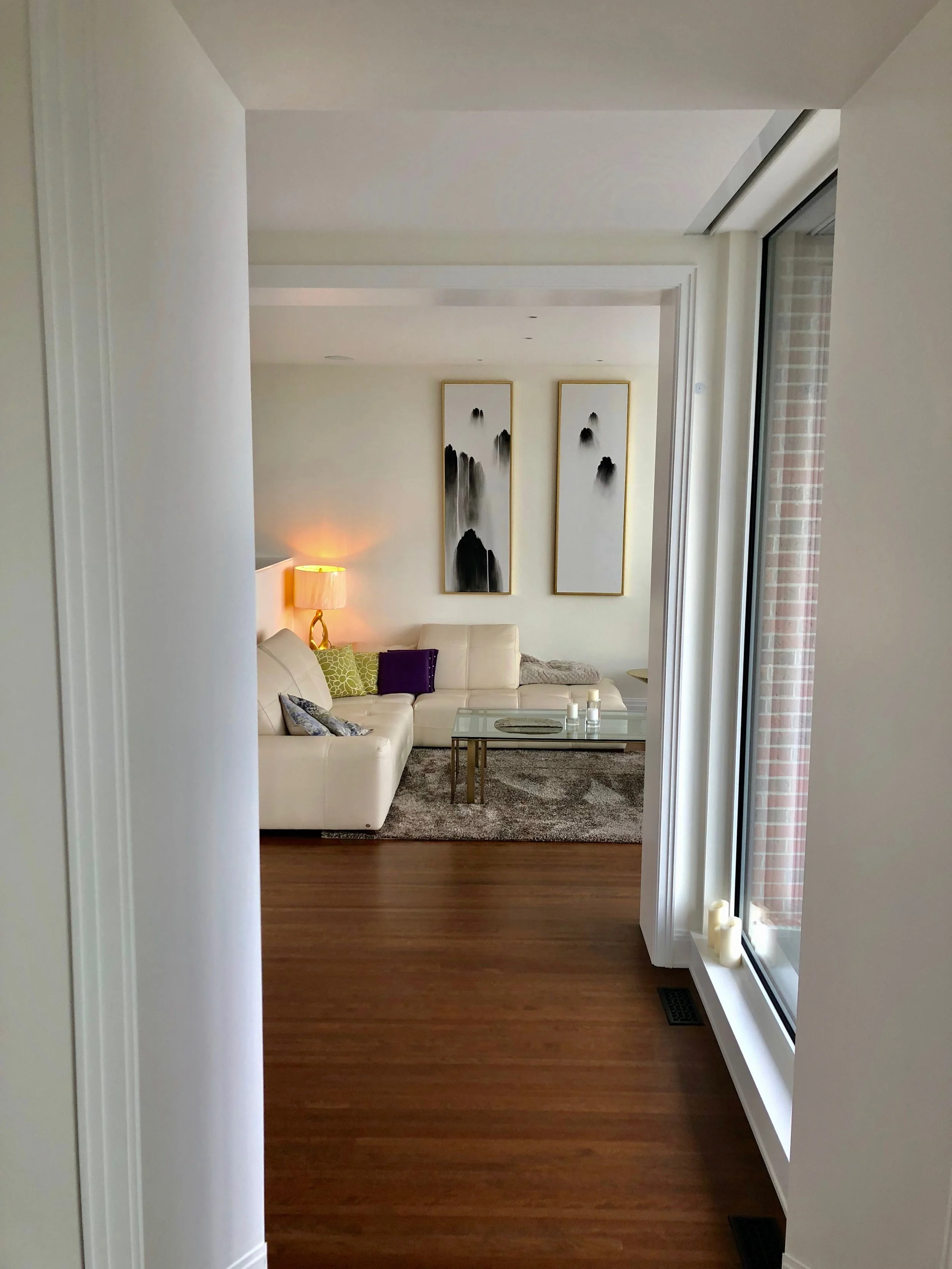 Living room with cream-colored sofa, abstract black and white artwork, a glass coffee table, area rug, lamp, and candles.