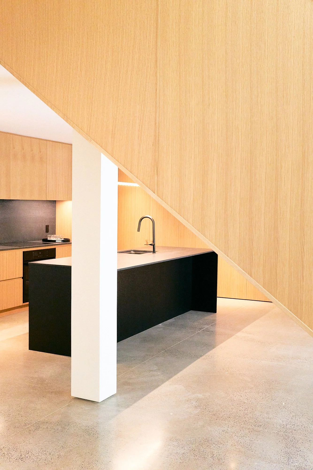 Modern kitchen with wooden cabinets, black island with a white countertop, a black sink and faucet, and a sloped wooden ceiling.