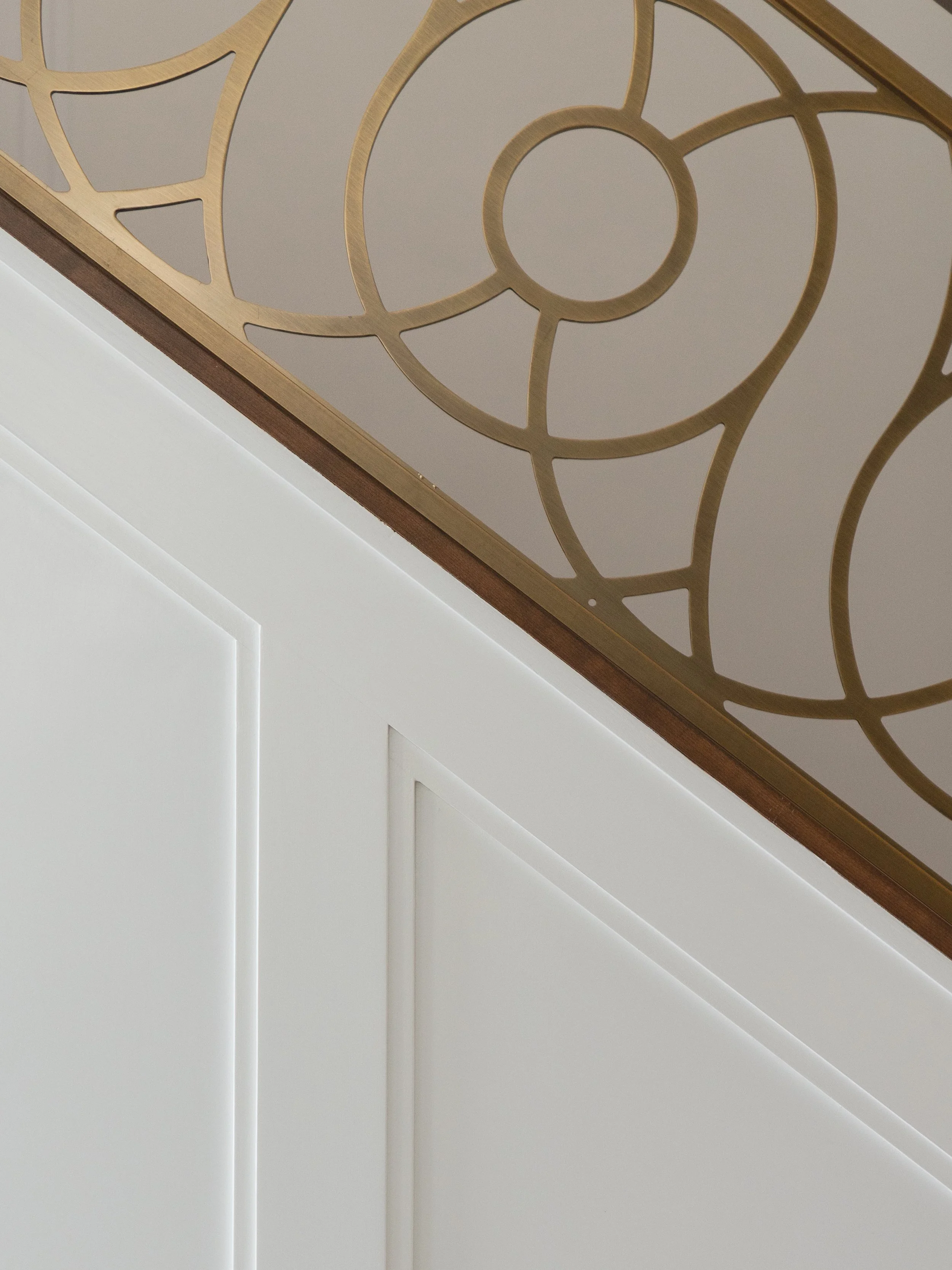 Close-up view of a ceiling with a decorative gold-colored metal panel featuring geometric circular patterns, and white wall paneling with subtle molding details.